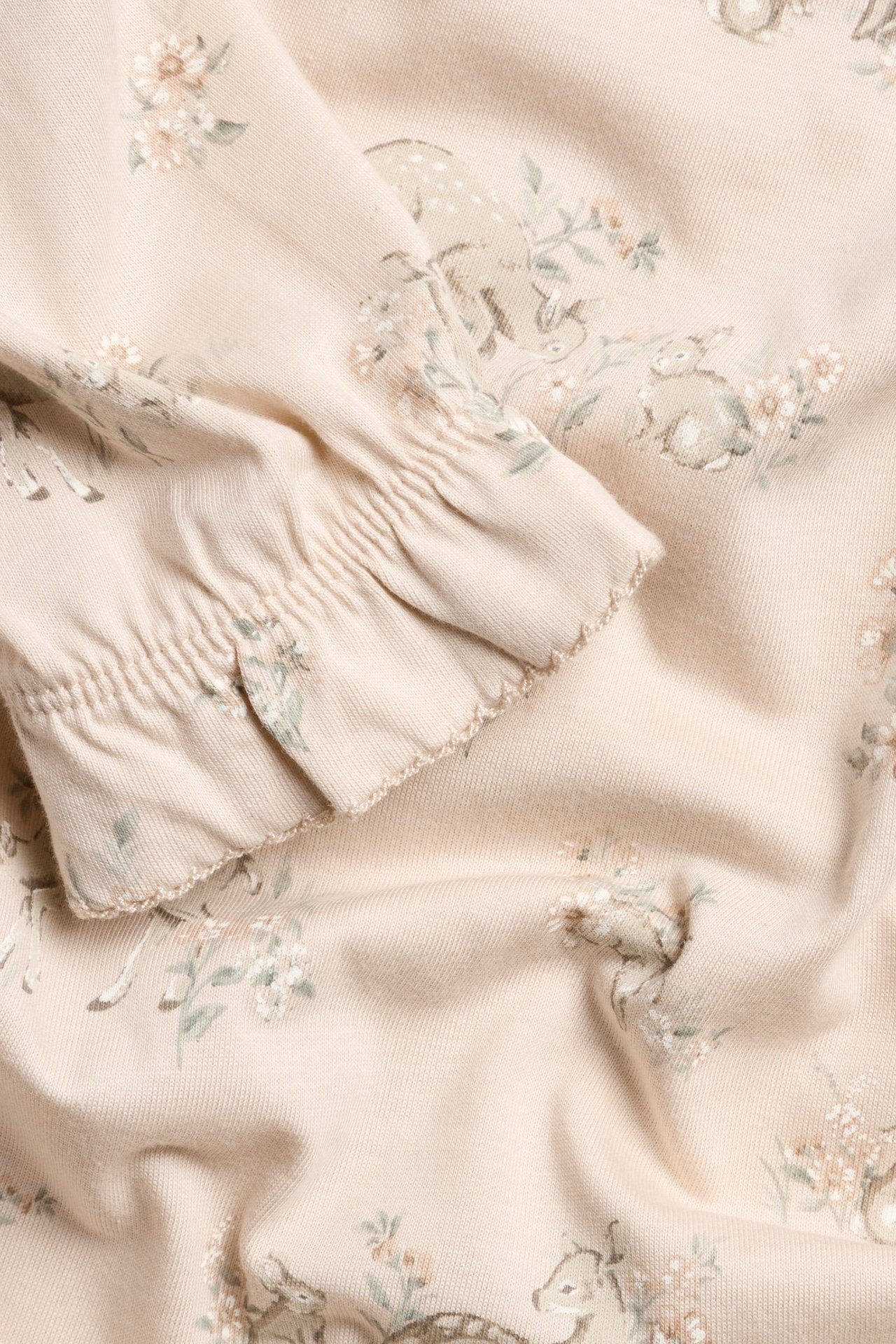 Nærbilde av lys rosa bomullsjersey nattkjole med blomster- og rådyrmønster og rynket mansjett.