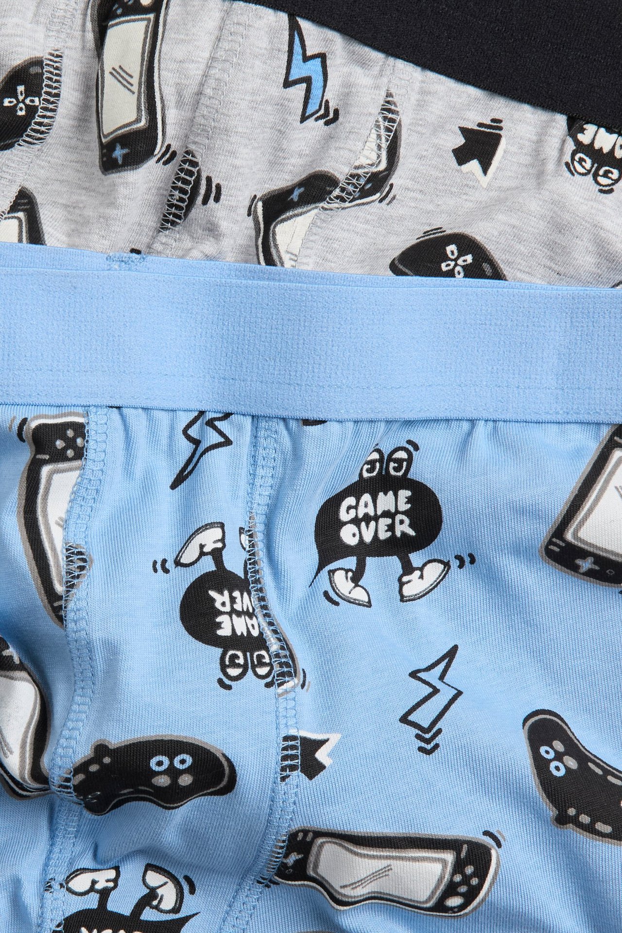 Zbliżenie na jasnoniebieskie bokserki dziecięce z wzorem gamingowym i jasnoszarą parą.