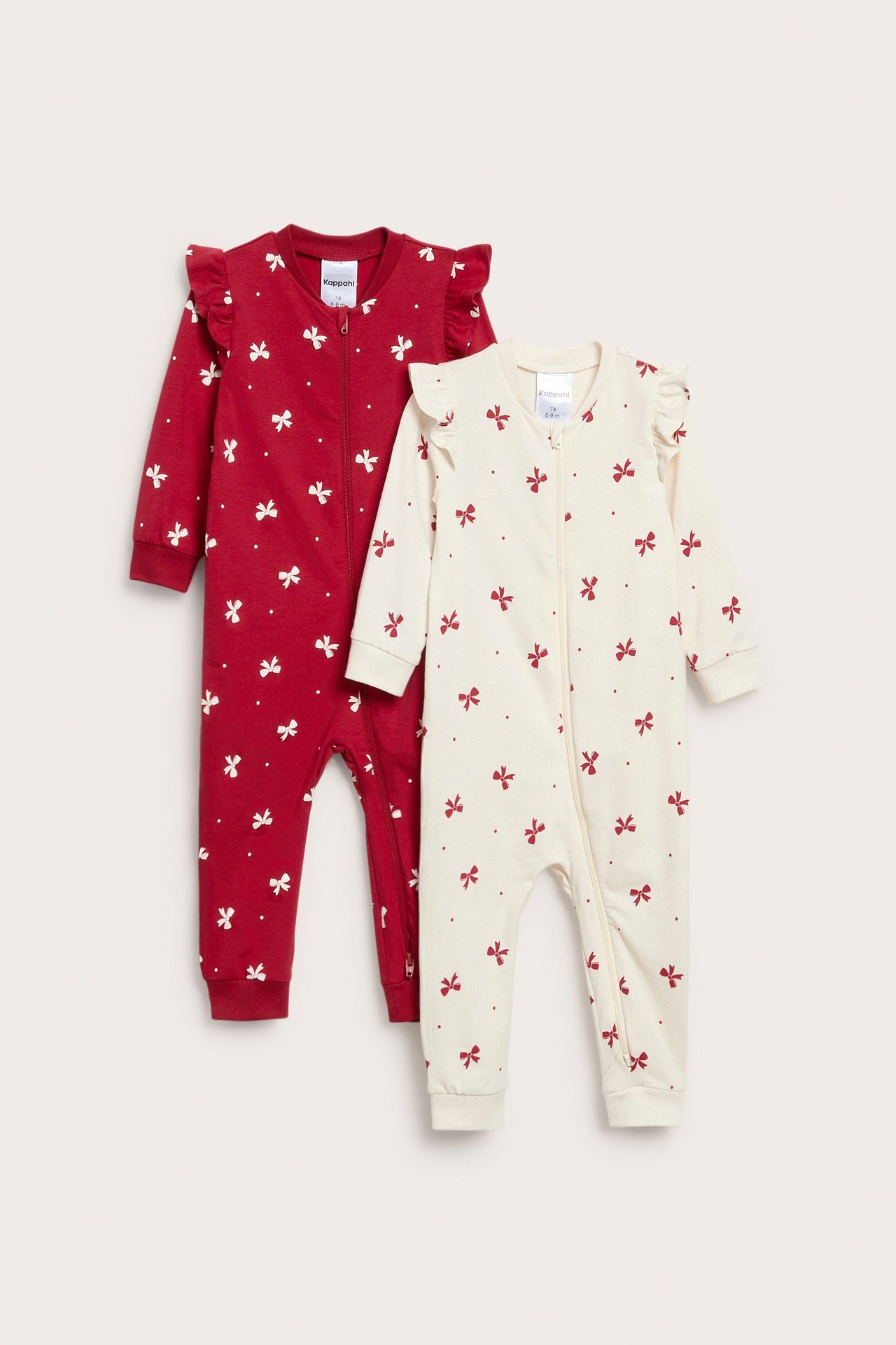 Frontvisning: To baby-pysjamaser. En rød med hvite sløyfer, en off-white med røde sløyfer, begge med volanger og toveisglidelås.