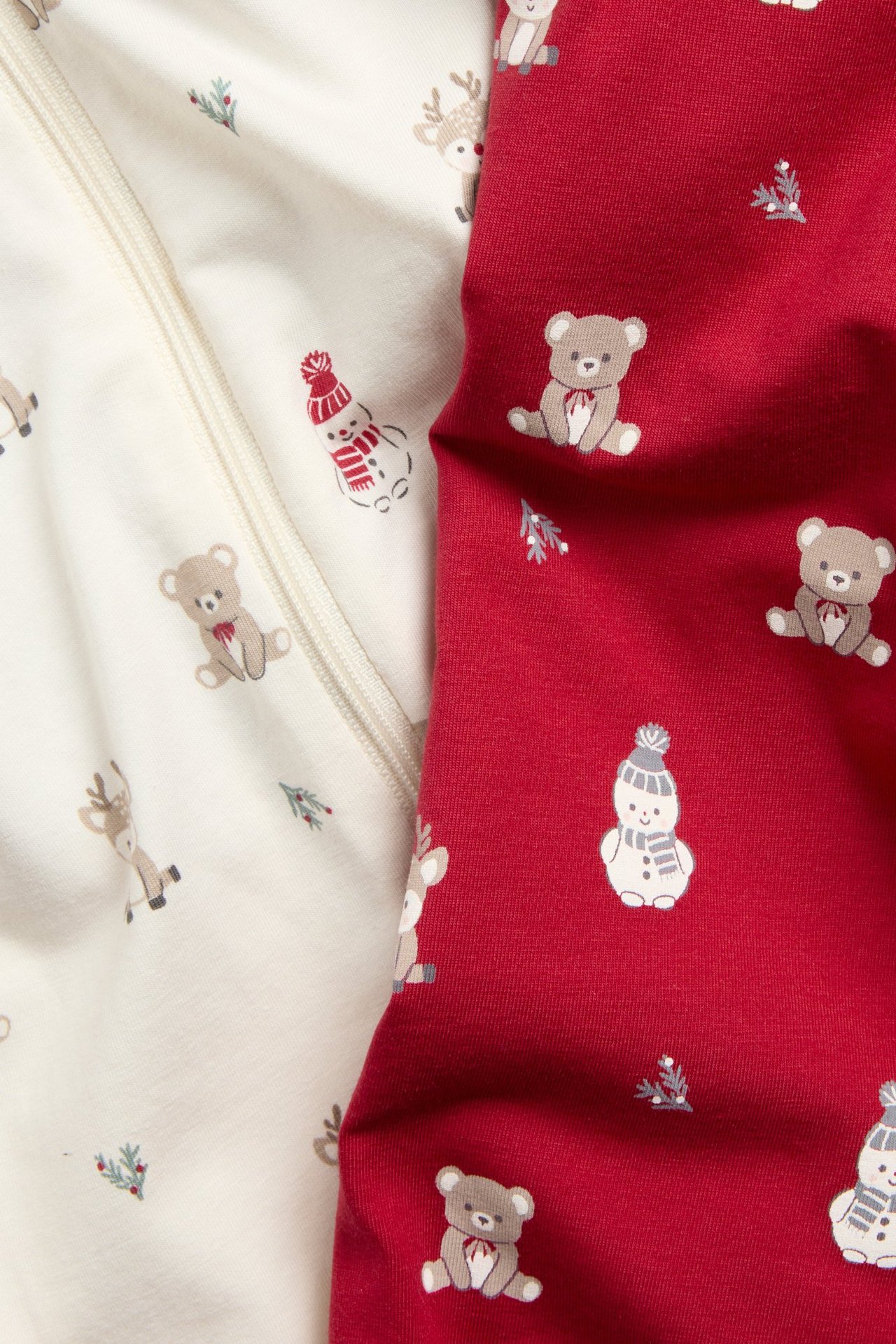 Zbliżenie na dwa wzorzyste pajacyki niemowlęce: ecru na zamek, czerwony, oba ze świątecznymi wzorami.