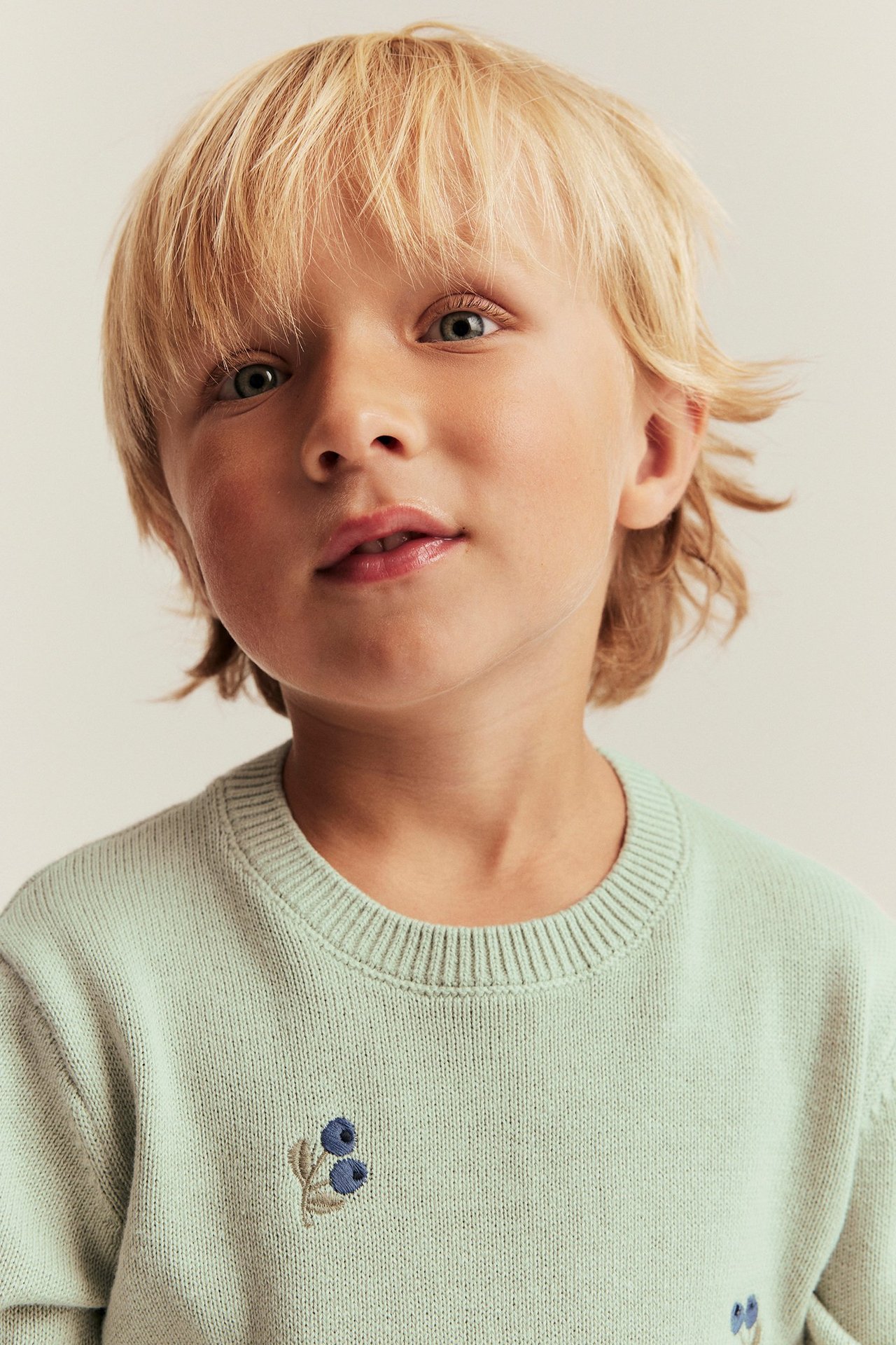 Lähikuva edestä, lapsi yllään vaaleanvihreä jacquard-neulepaita mustikkakirjailulla.