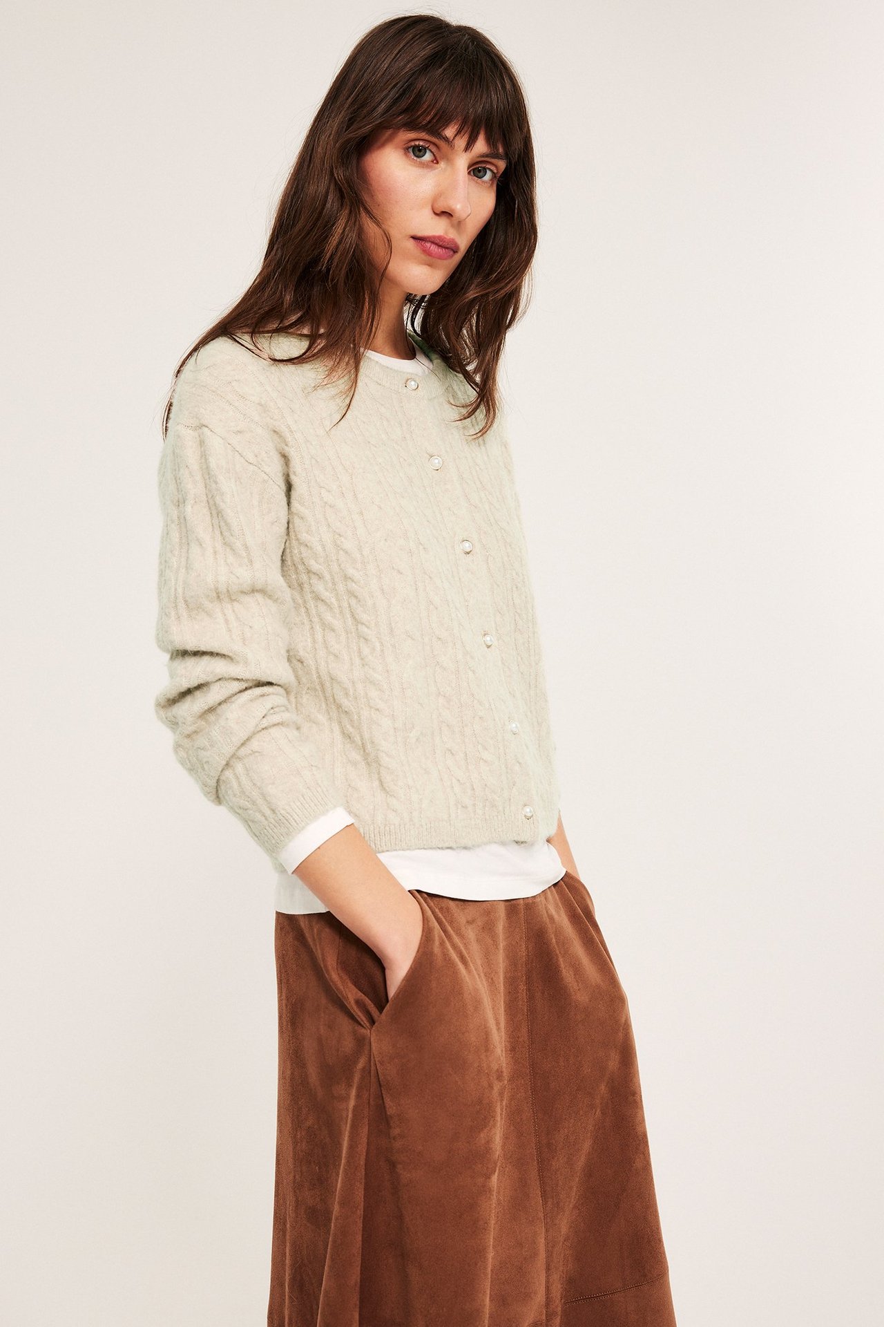 Naismalli käyttää beigeä palmikkoneuletakkia helmineuluksilla, päällä valkoinen toppi, etunäyttö.