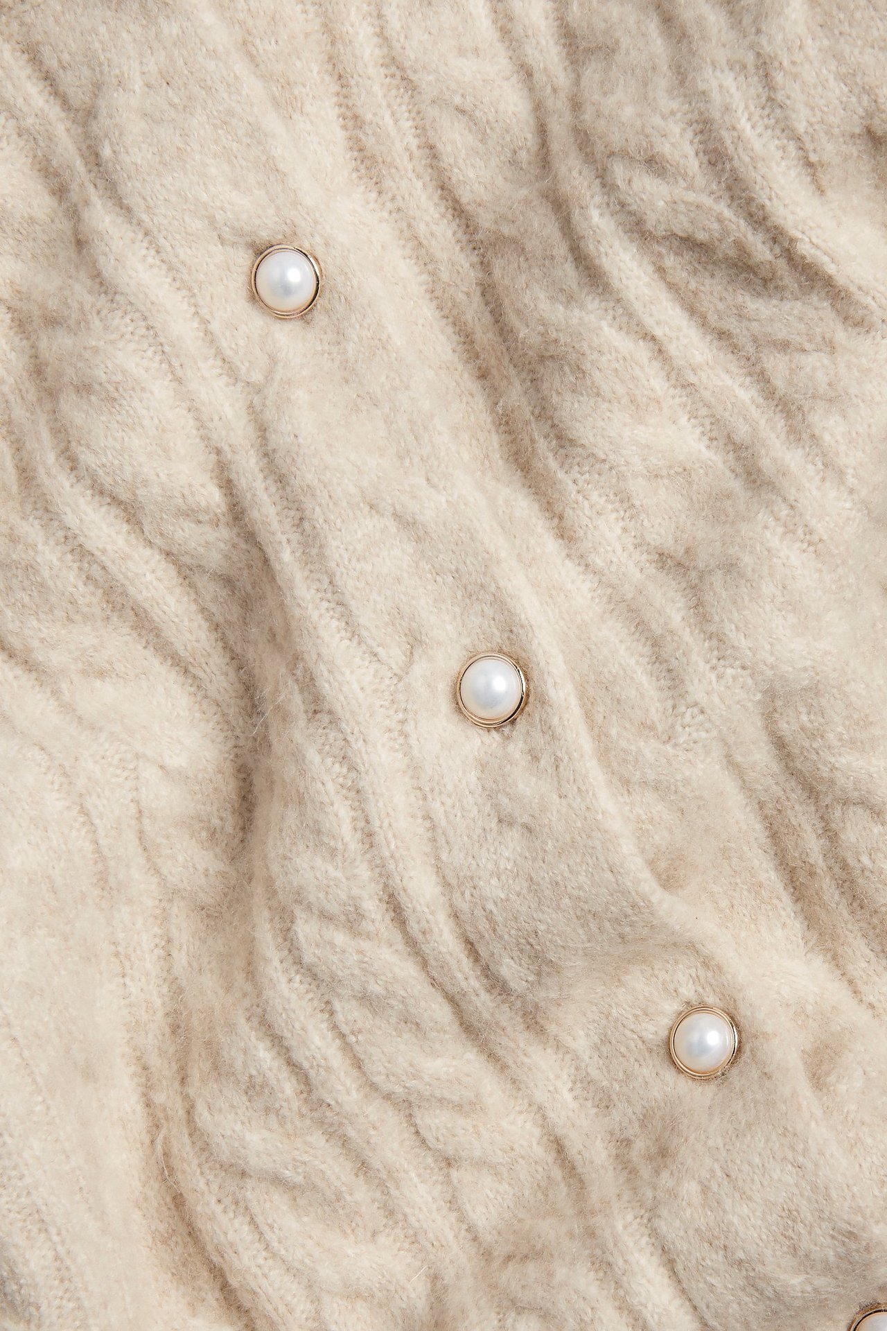 Zbliżenie beżowego kardiganu o splocie warkoczowym z okrągłymi guzikami z masy perłowej i złotymi obwódkami.