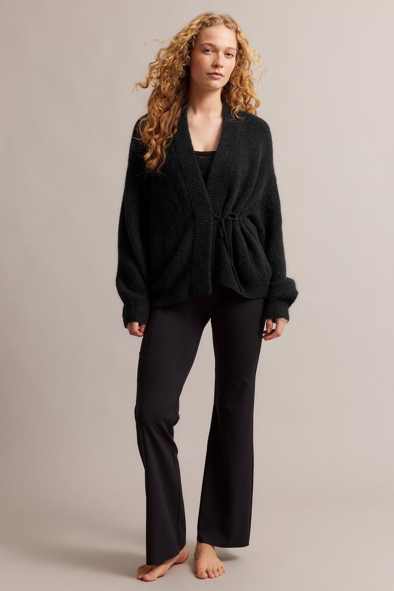 Forfra: Kvinne i svart ullmiks-knytekardigan, svart singlet og svarte utsvingte bukser.