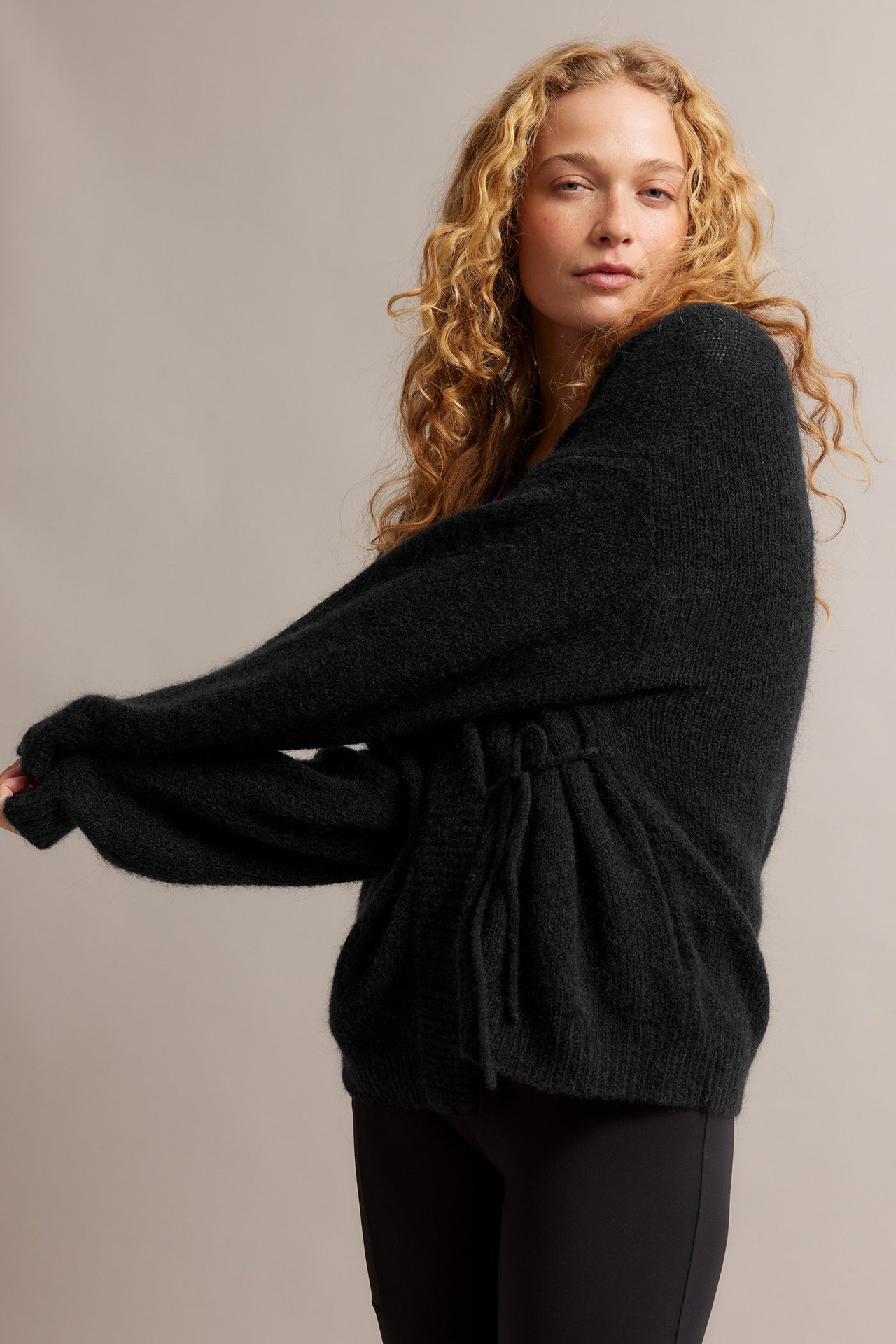 Naisen sivukuva mustassa villasekoitekardigaanissa, jossa solmimisnauhat, ja mustissa leggingseissä.