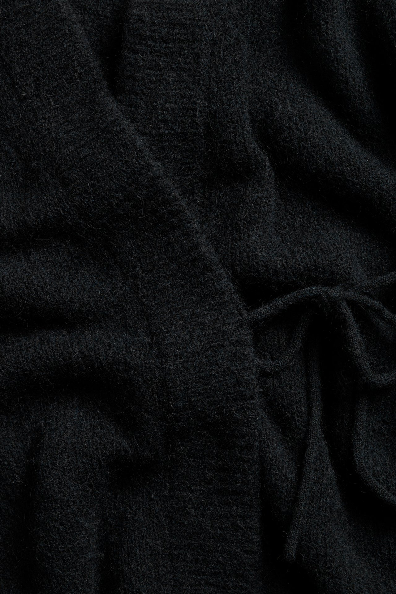 Lähikuva mustasta villasekoitejakista, jossa on solmittava nauha ja näkyvä pörröinen rakenne.