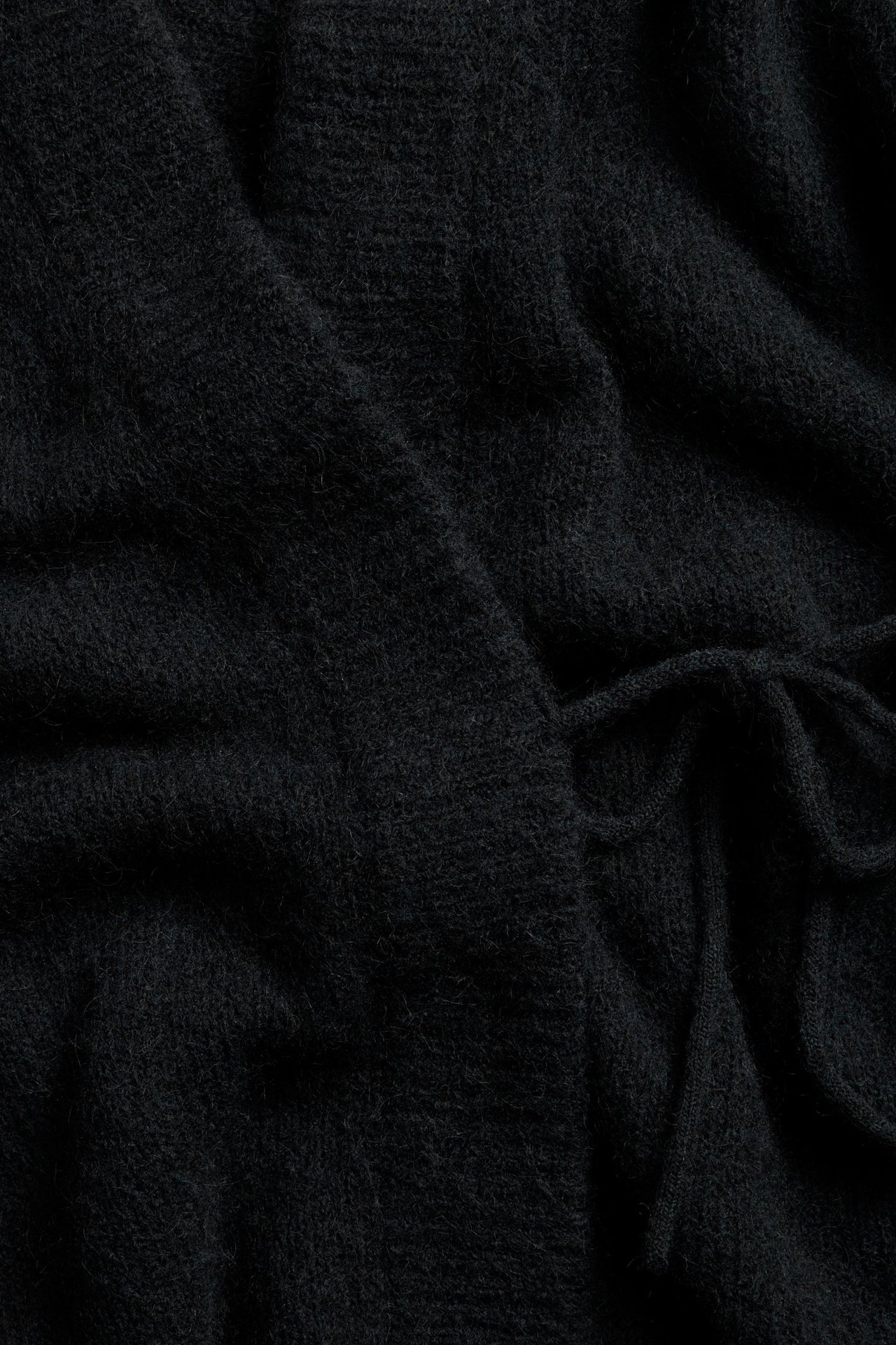 Zbliżenie czarnego swetra z domieszką wełny, z widocznym wiązaniem, ukazujące puszystą teksturę.