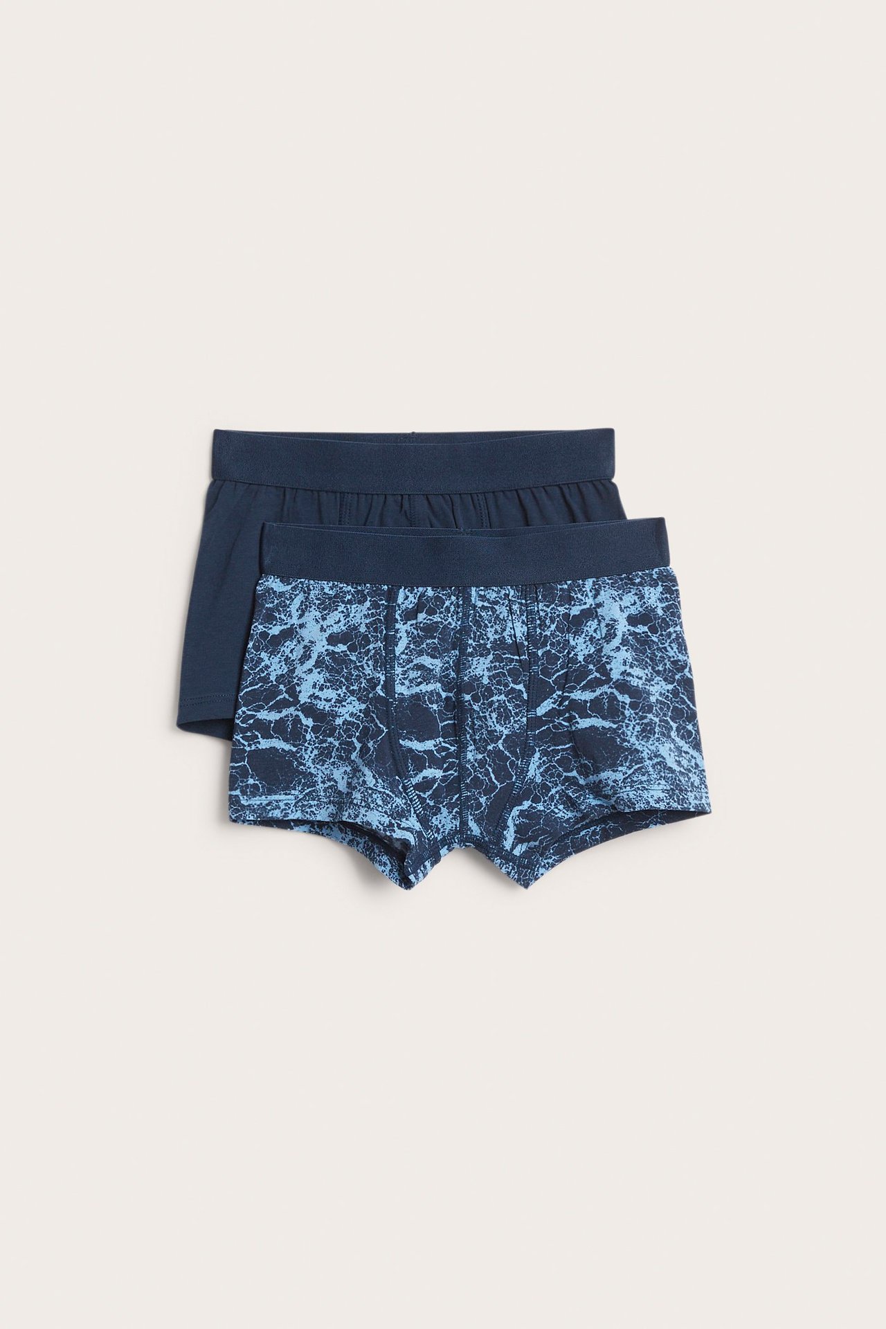 Forfra, to par mørkeblå boksershorts for barn, en mønstret og en ensfarget, med elastisk linning.