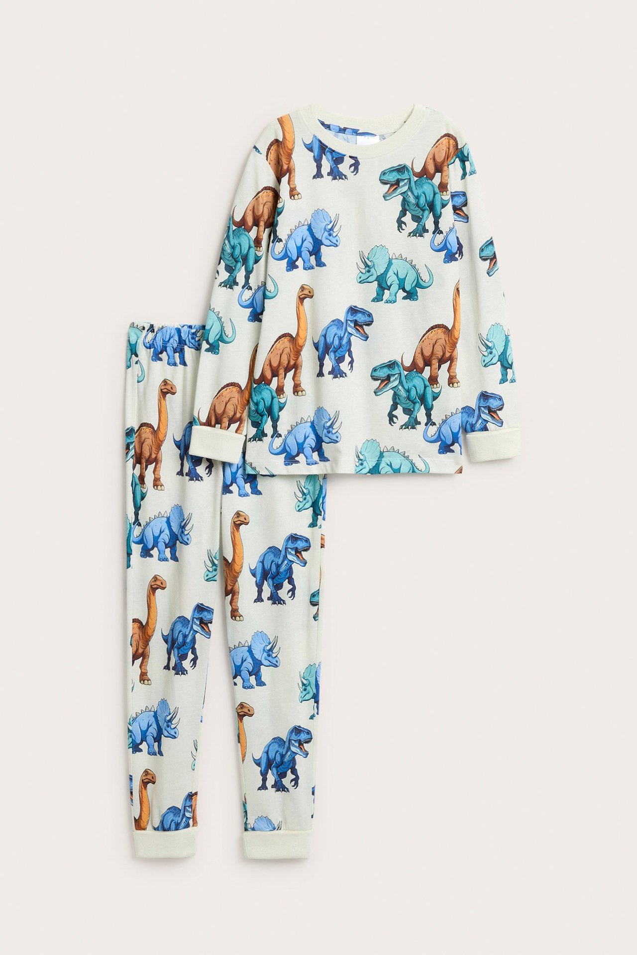 Edestä kuvattu luonnonvalkoinen puuvillapyjama dinosauruskuviolla, pitkillä hihoilla ja resoreilla lapsille.
