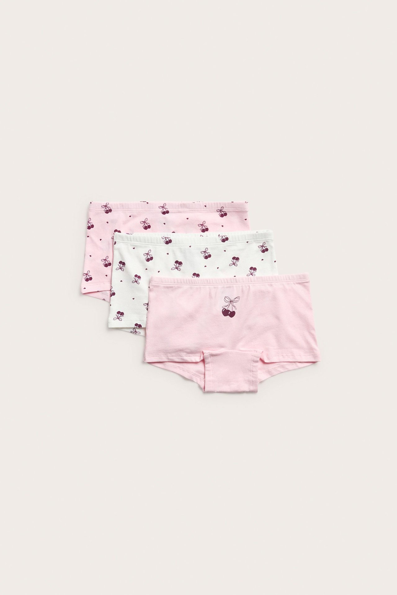 Widok z góry na trzy bawełniane bokserki dziecięce, różowe i białe w wiśniowe wzory.