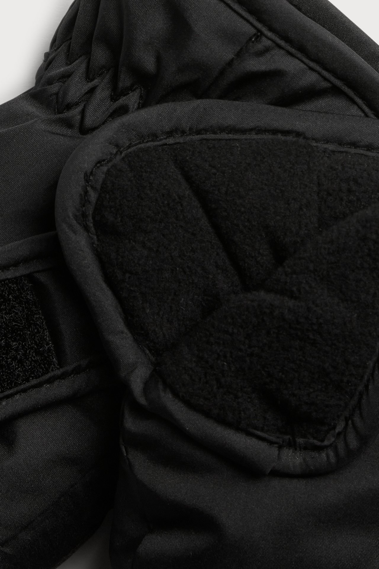 Lähikuva mustasta pehmustetusta käsineestä, jossa on fleece-kämmen ja tarranauha.