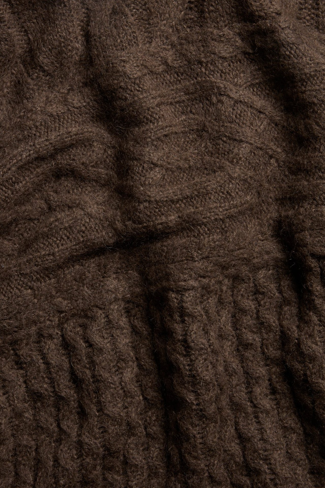 Zbliżenie na ciemnobrązowy sweter z mieszanki wełny, z widocznymi warkoczowymi i prążkowanymi splotami.