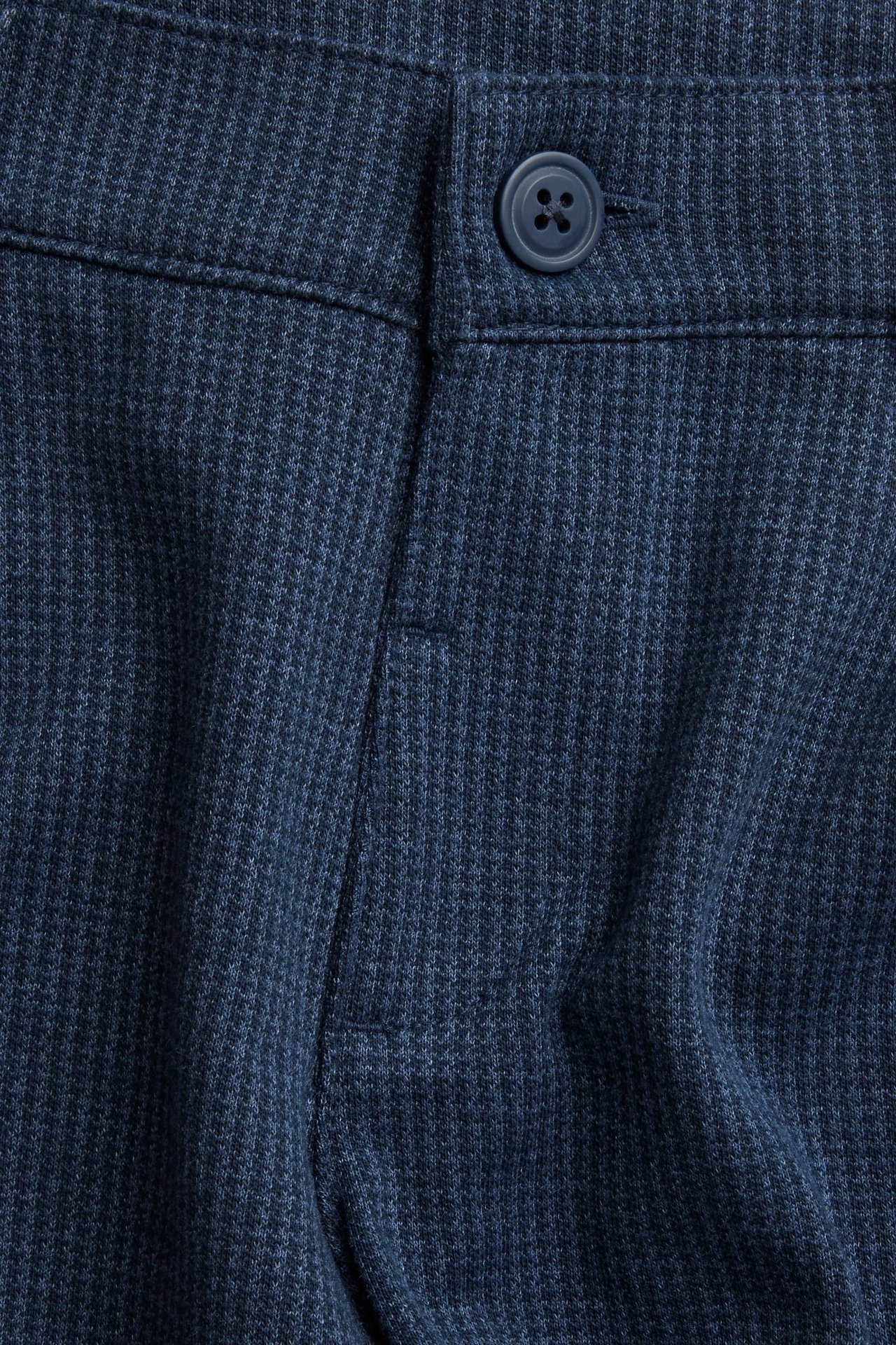 Zbliżenie na ciemnoniebieskie wzorzyste spodnie wizytowe dziecięce z mieszanki bawełny, z guzikiem i imitacją rozporka.