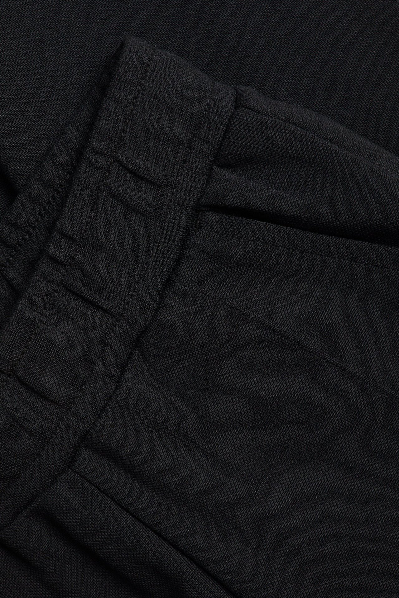 Zbliżenie czarnych spodni dresowych z elastyczną talią i boczną kieszenią.