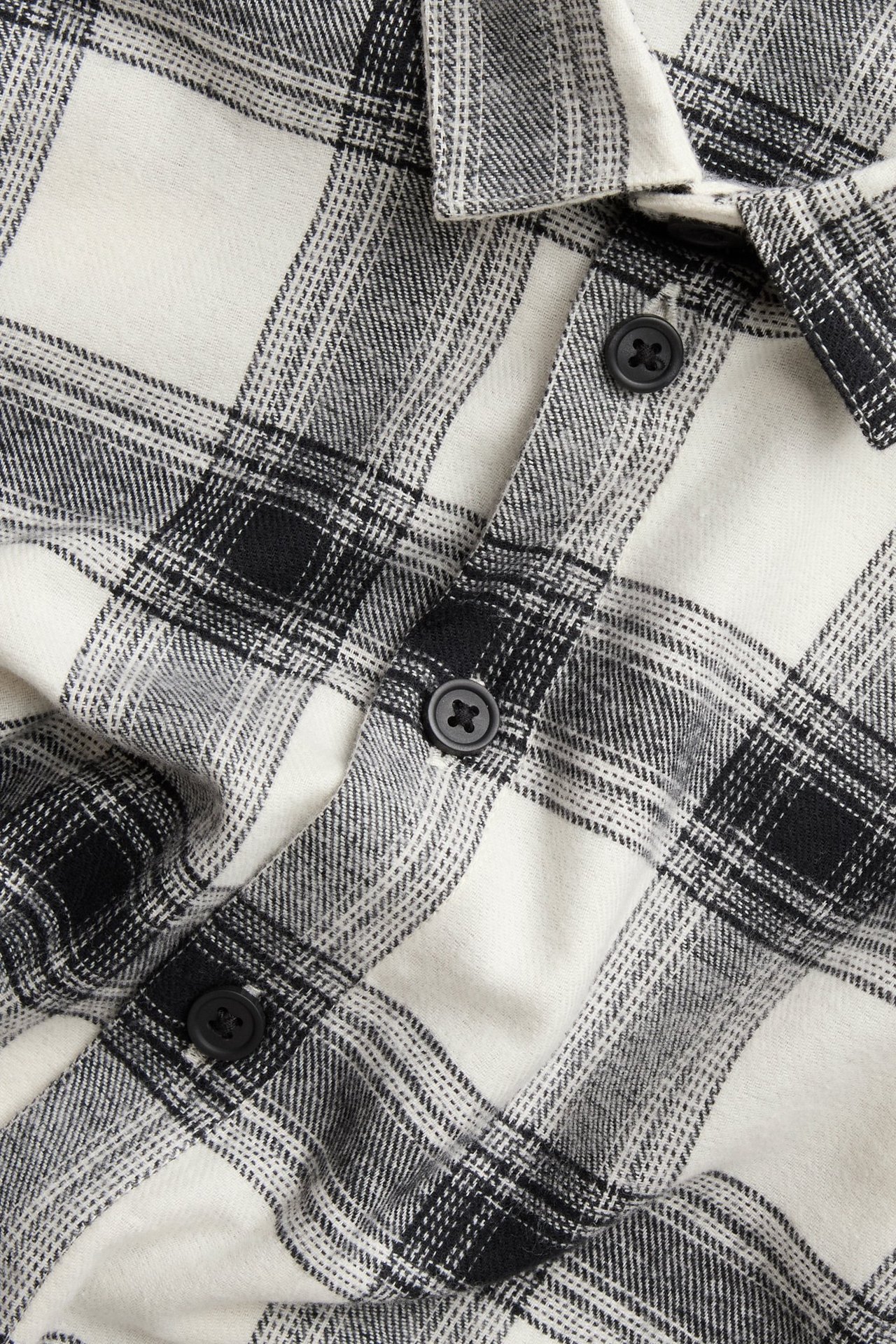 Zbliżenie przodu dziecięcej, jasnobeżowej i czarnej, kraciastej koszuli flanelowej z bawełny z czarnymi guzikami.