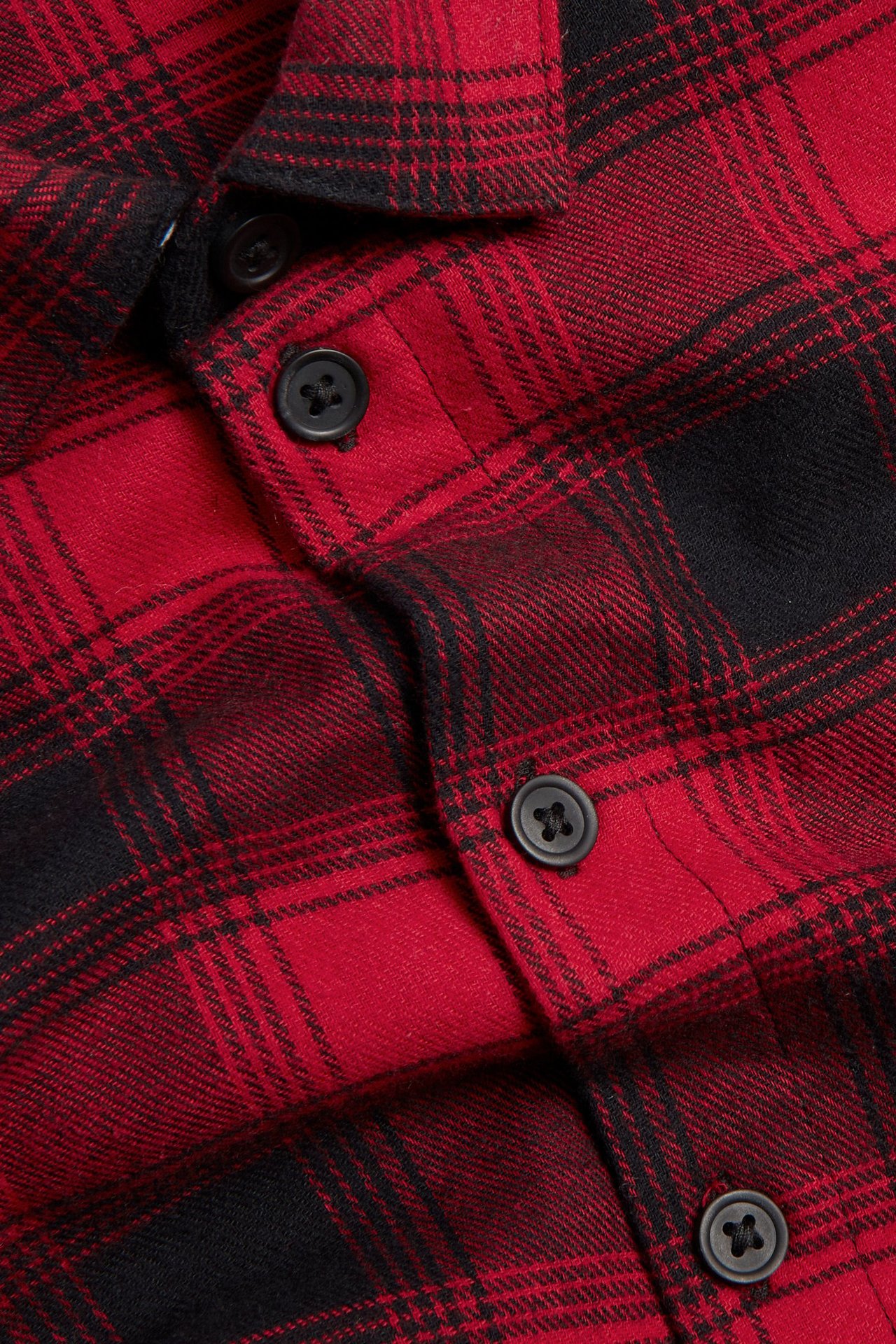 Zbliżenie na czerwoną i czarną flanelową koszulę w kratę z bawełny z czarnymi guzikami.