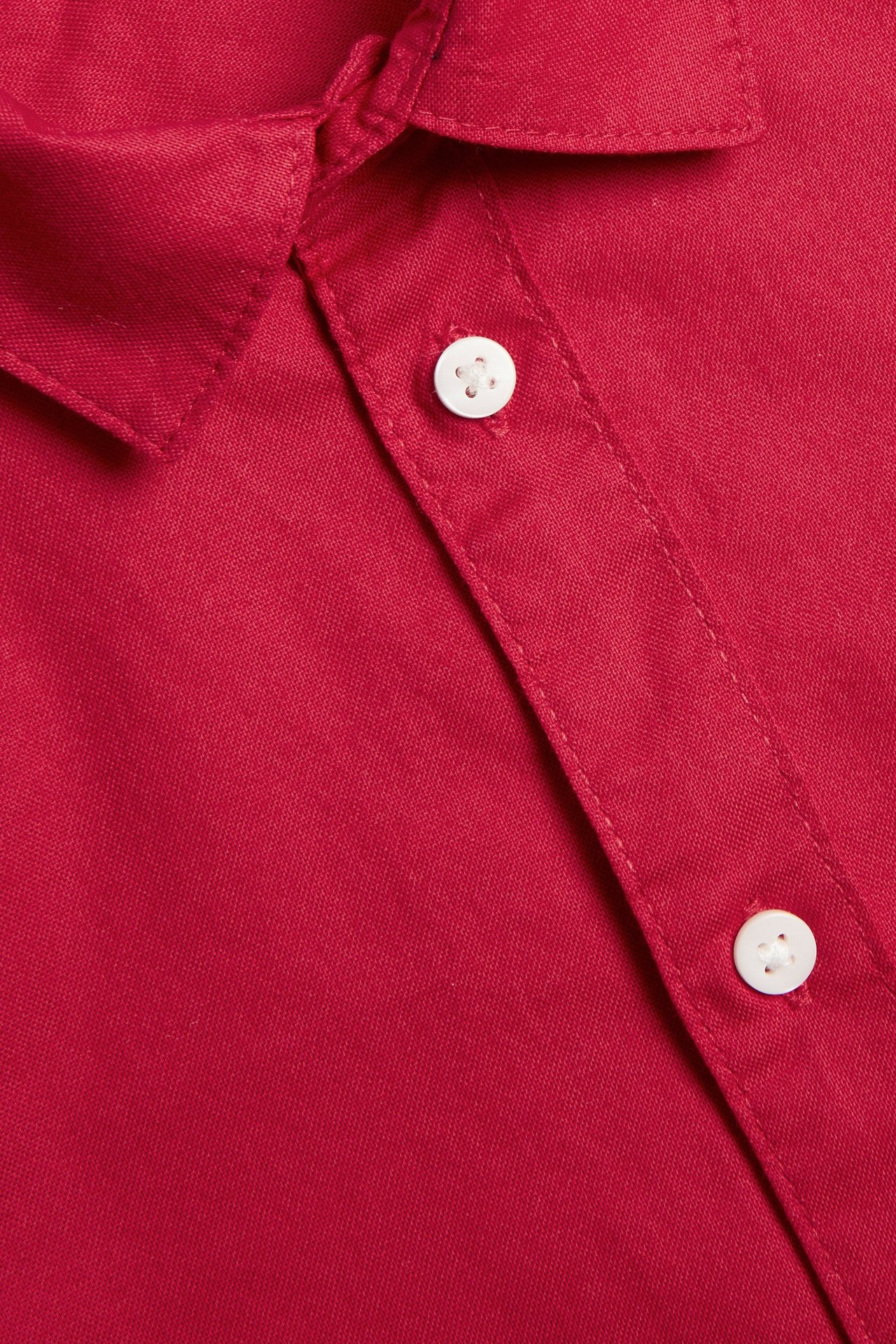 Zbliżenie na czerwoną koszulę Oxford z bawełny, przedstawiające kołnierz i białą listwę z guzikami.