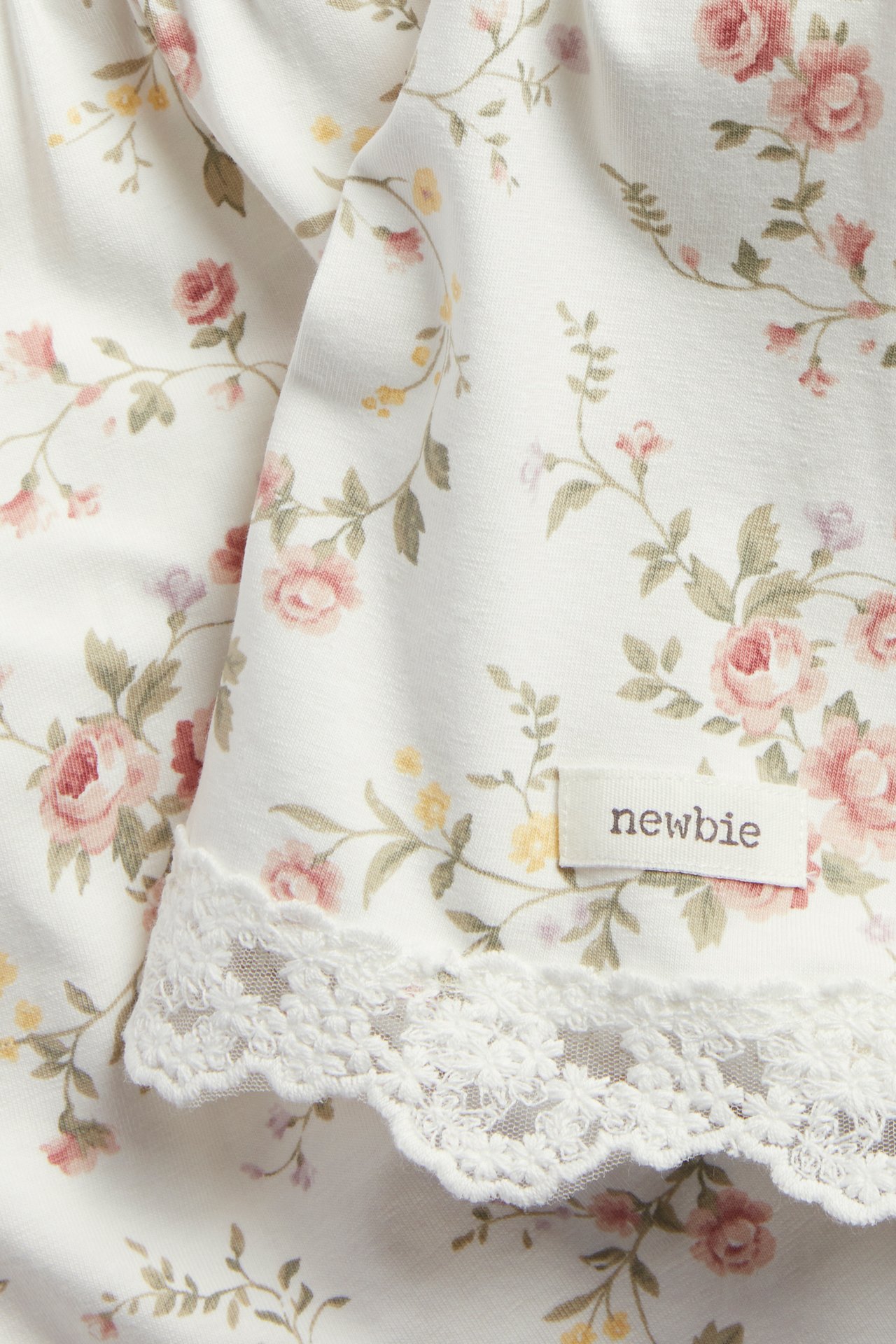 Nærbilde av en kremfarget blomstret strikkekjole med rosa roser og blondekant.