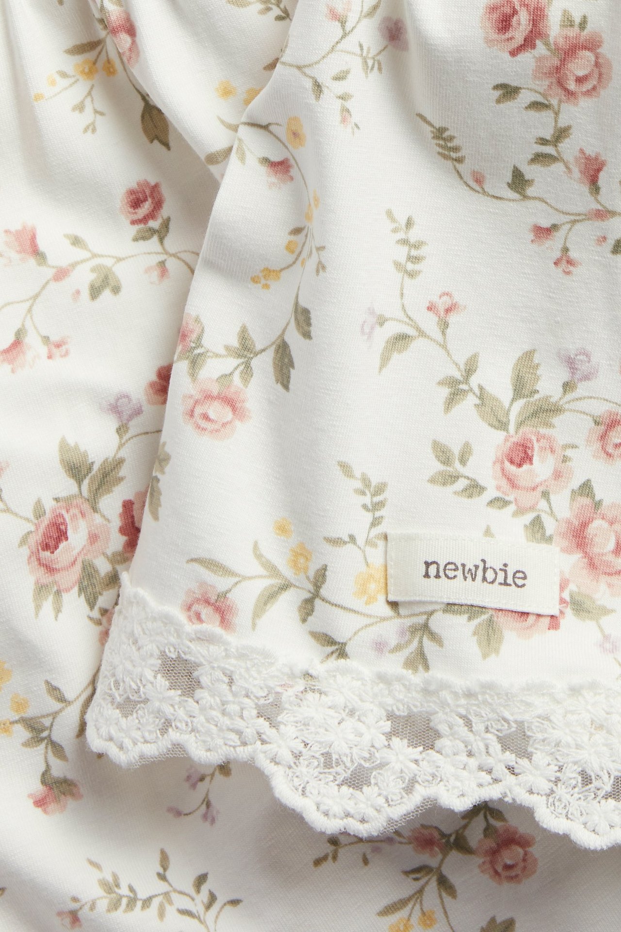 Nærbilde av en kremfarget blomstret strikkekjole med rosa roser og blondekant.