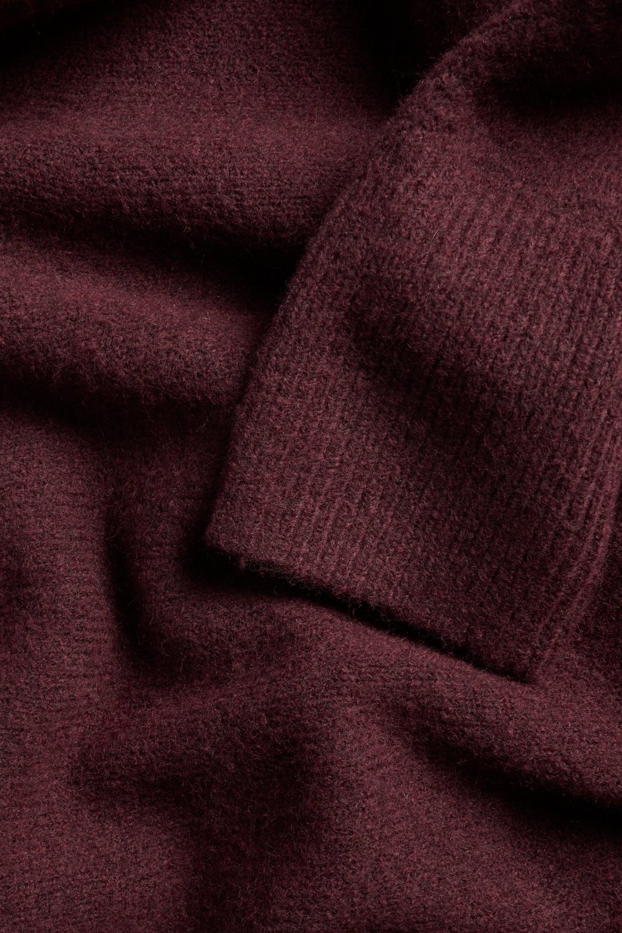 Zbliżenie na ciemnoczerwoną, drobno dzianą sukienkę z widocznym ściągaczem.