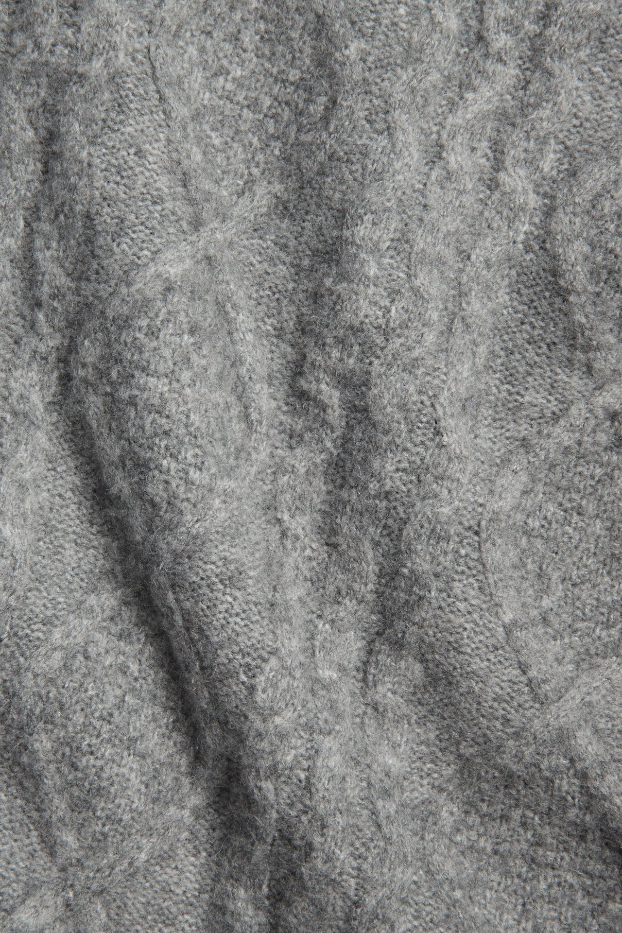 Zbliżenie szarego, melanżowego swetra warkoczowego z teksturą.
