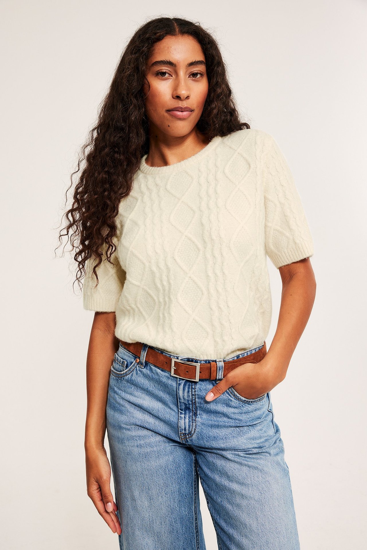 Kabelstickad tröja i ljusbeige med strukturmönster, kvinna, kort ärm, över jeans.