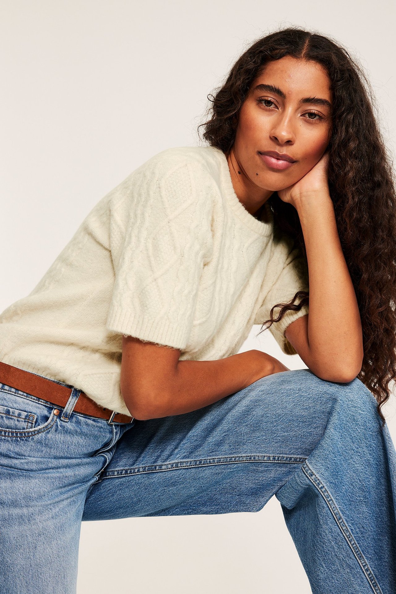 Kvinna i beige kabelstickad tröja, loose fit, med struktur, över jeans.
