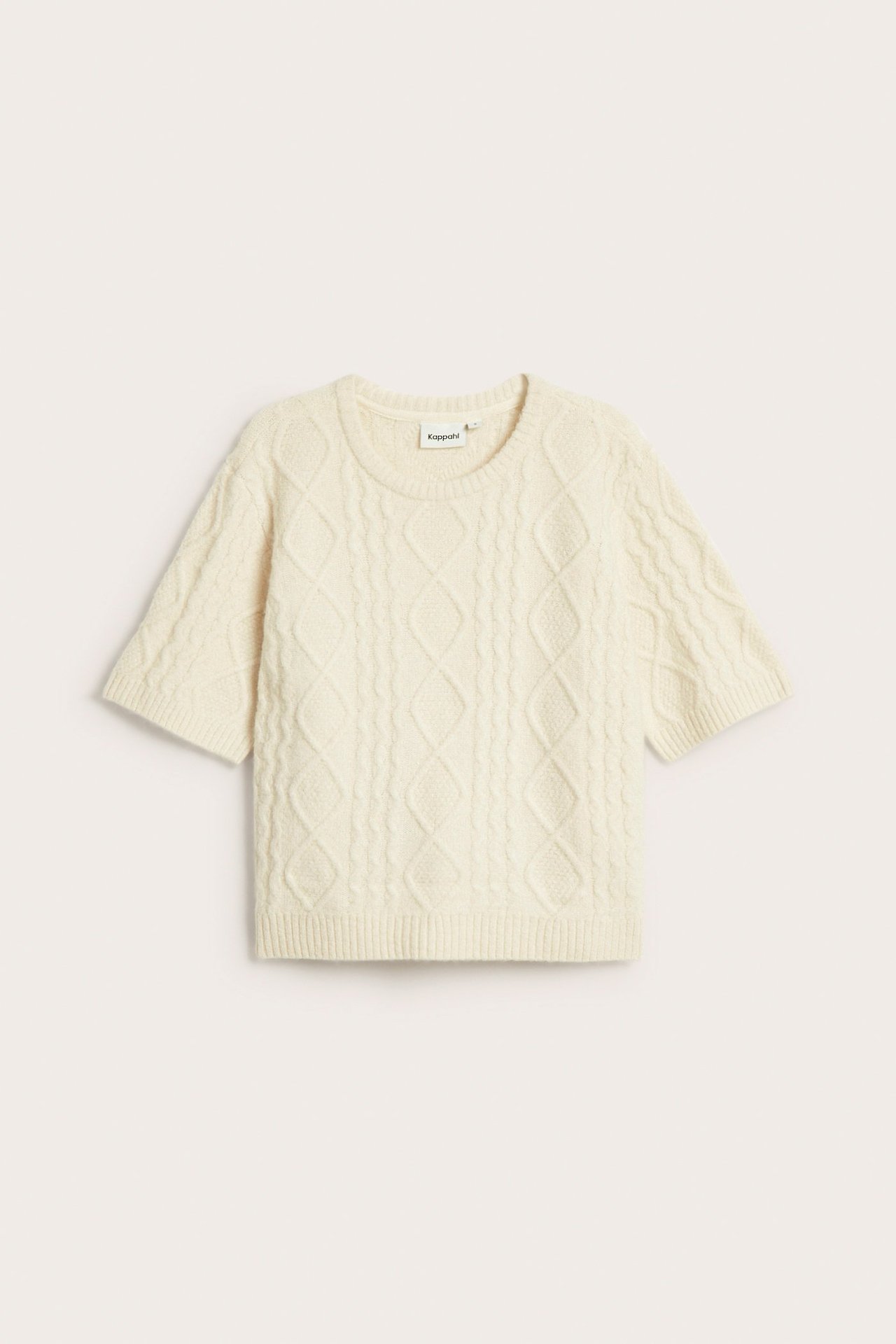 Framsida av en ljusbeige kabelstickad tröja med rundhals och korta ärmar.