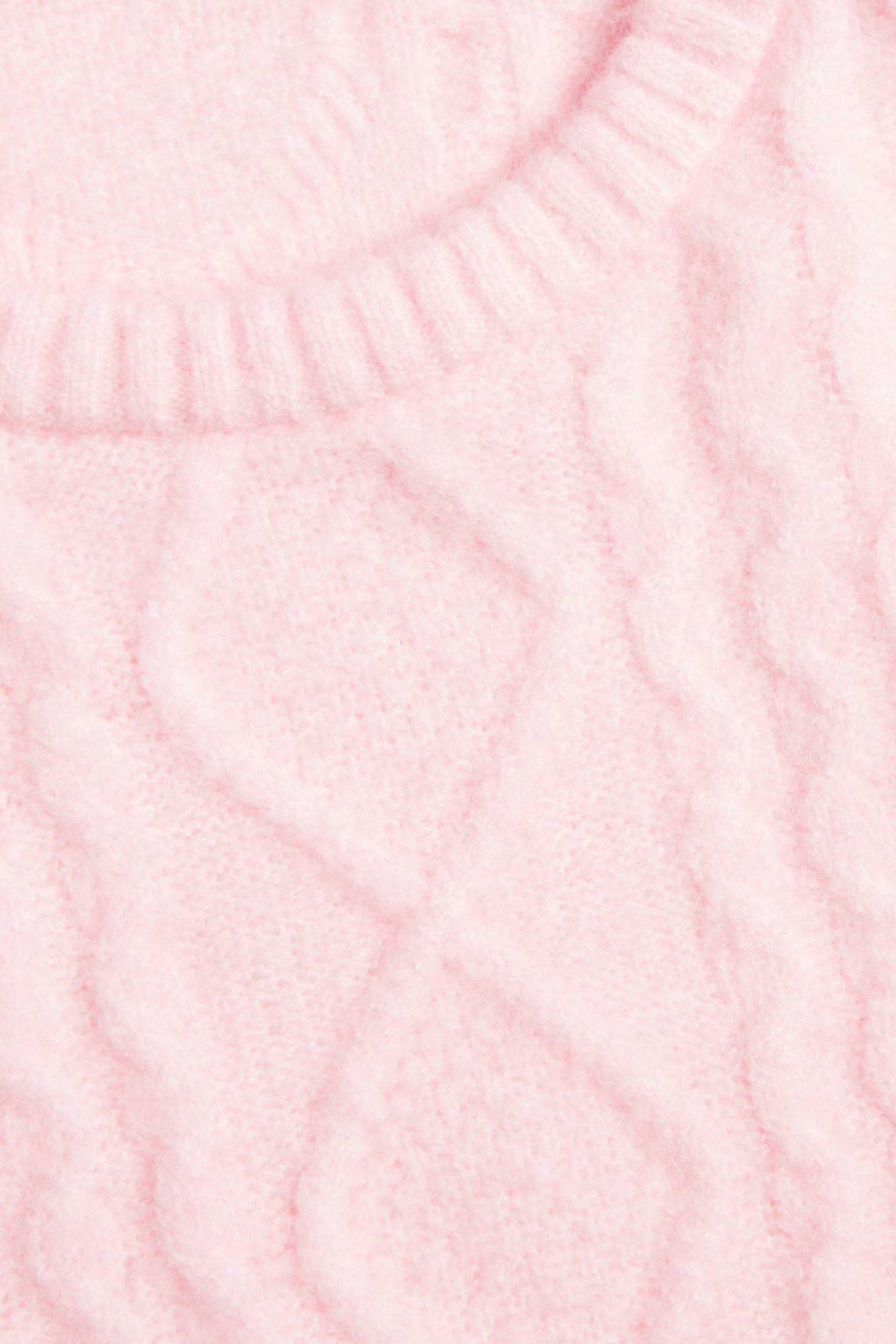 Zbliżenie jasnoróżowego swetra w warkocze z prążkowanym okrągłym dekoltem.