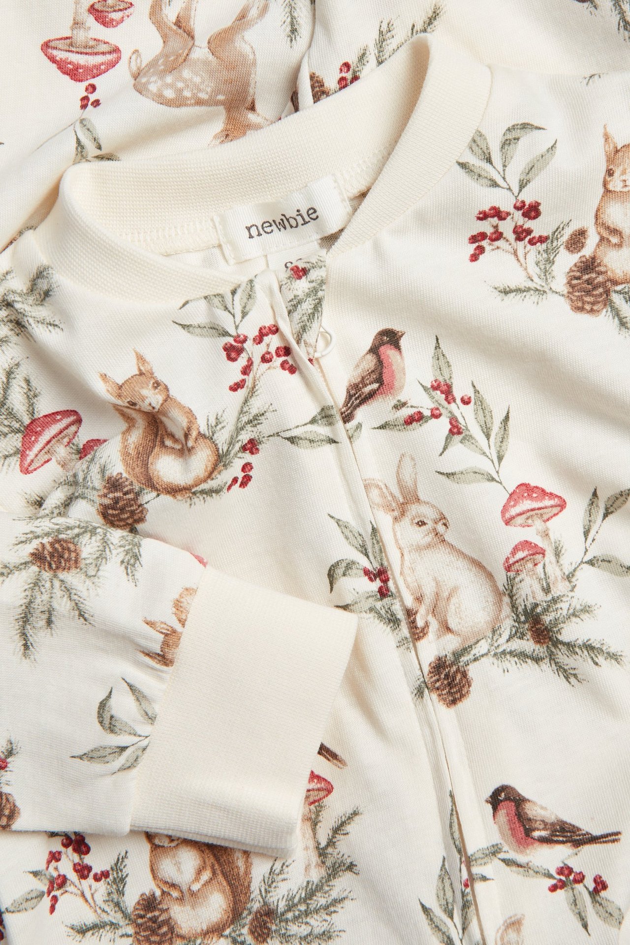 Närbild av babypyjamas i offwhite med juligt djurmönster och tvåvägsdragkedja.