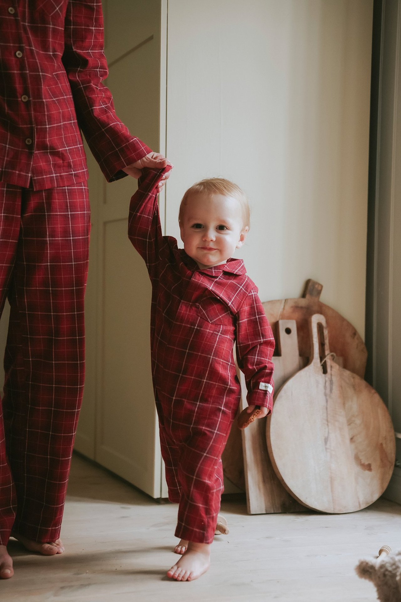 Edestä: vauva punaisessa ruudullisessa flanellipyjamassa neppareilla, pitää aikuisen kättä.