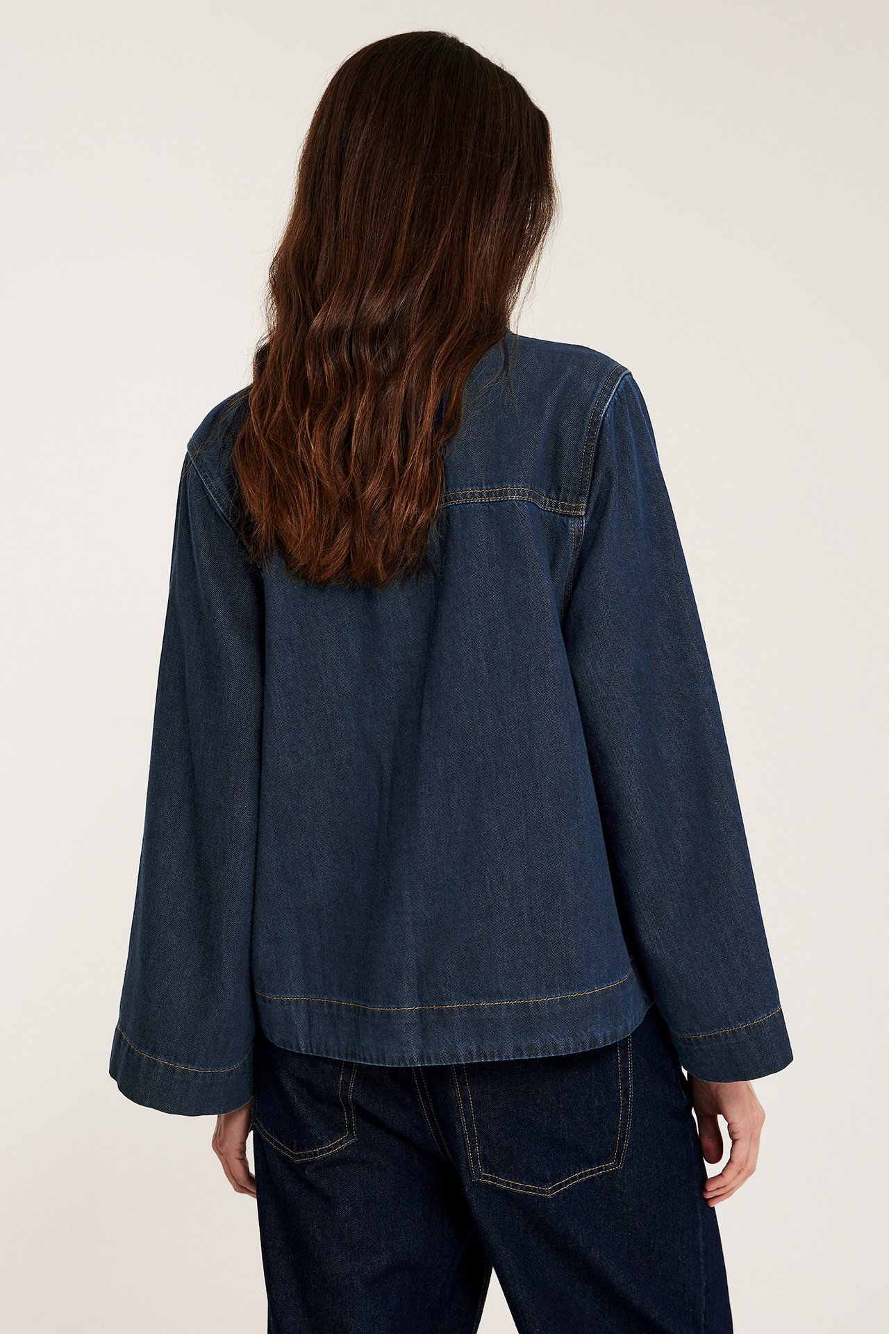 Ryggvy av kvinna i mörkblå popoverskjorta i denim med vida ärmar och matchande jeans.