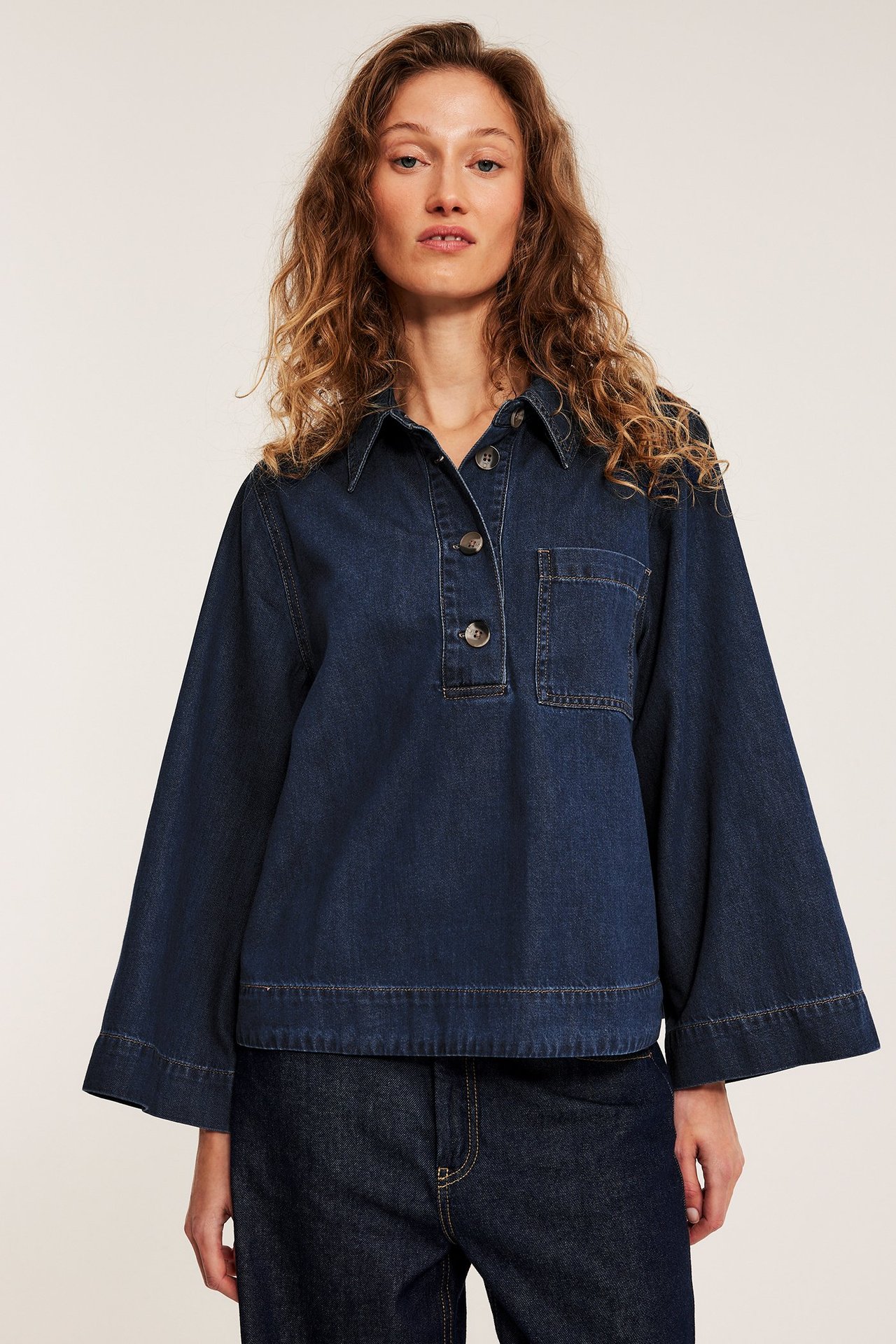 Forfra: Kvinne i mørk denimskjorte med skilpaddemønstrede knapper, vide ermer og brystlomme.