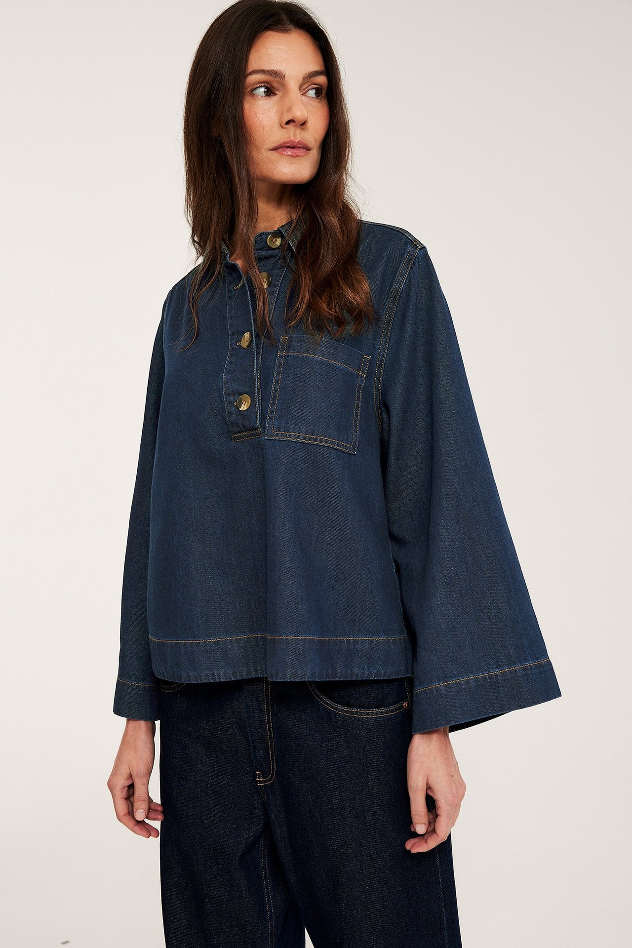 Kobieta w ciemnej dżinsowej koszuli popover z guzikami szylkretowymi, szerokimi rękawami i ciemnymi dżinsami.