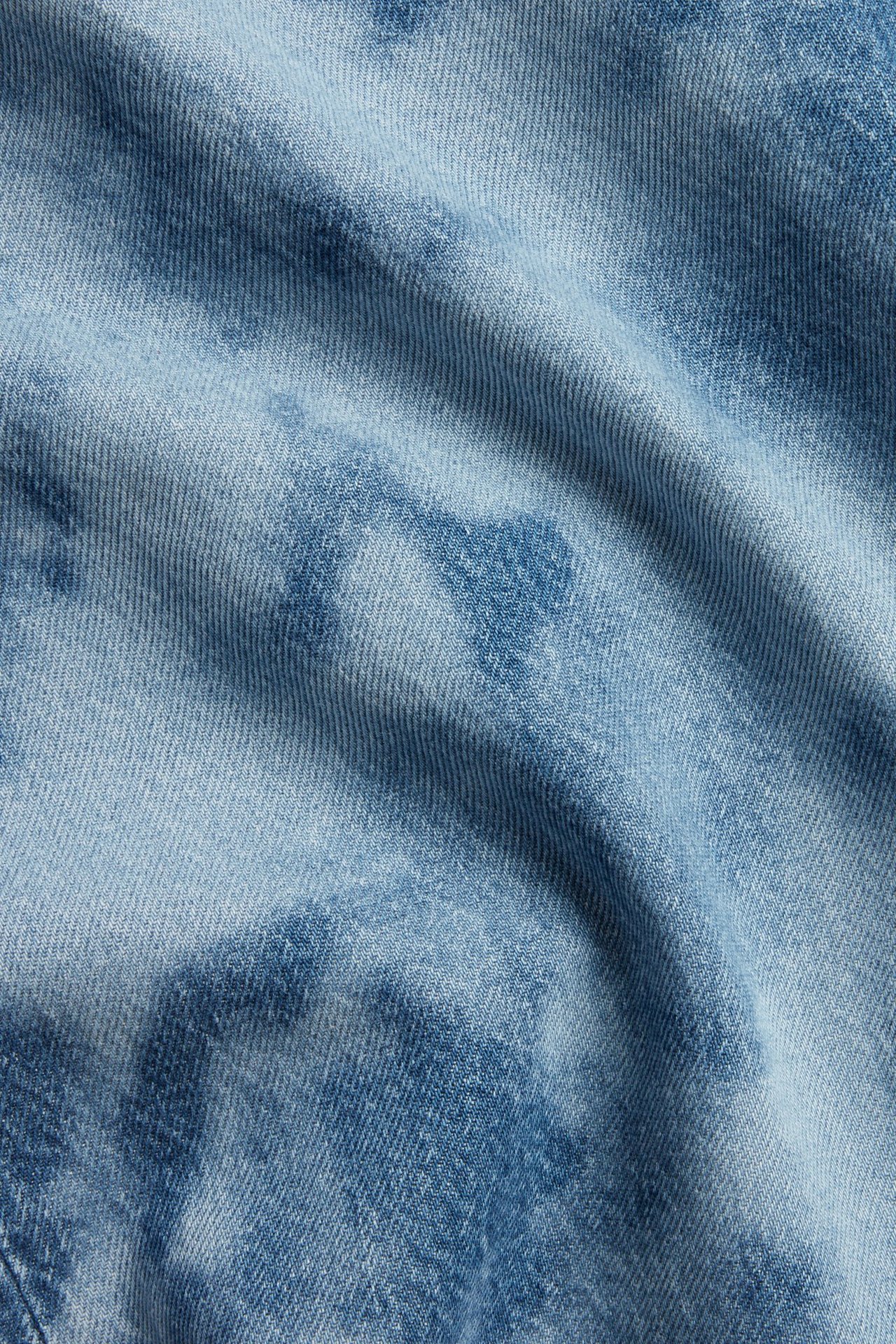 Zbliżenie na jasny denimowy materiał szerokich jeansów z wysokim stanem, z marmurkowym wzorem batik.