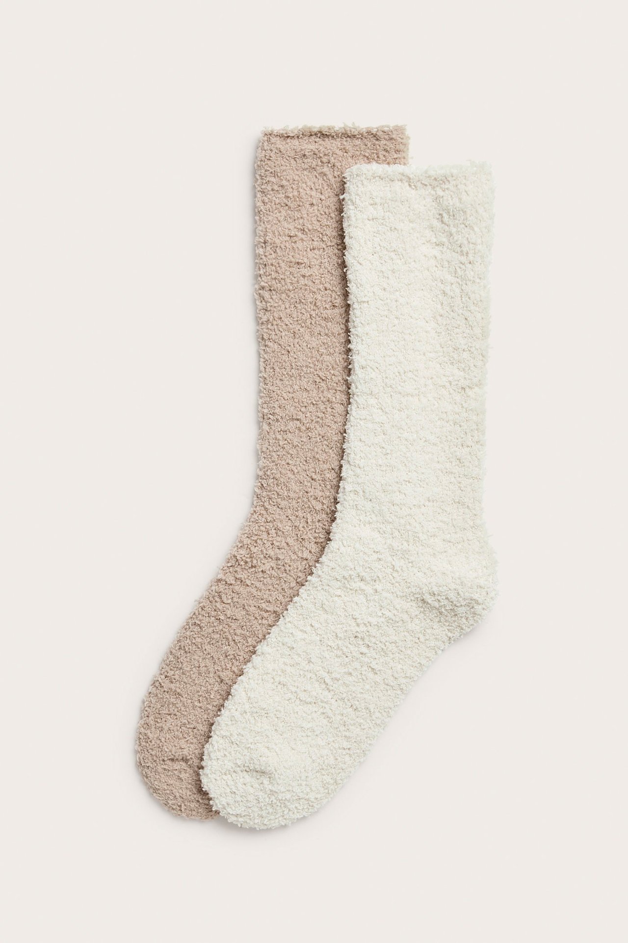 Widok z góry na dwie puszyste, jednokolorowe skarpetki: jedną beżową i jedną ecru.