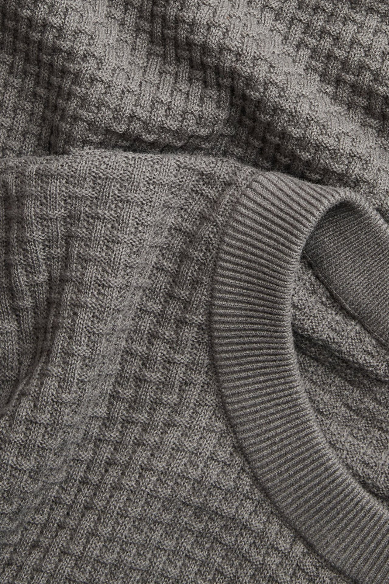 Zbliżenie szarego bawełnianego swetra z dzianiny o strukturalnym wzorze i prążkowanym dekolcie.