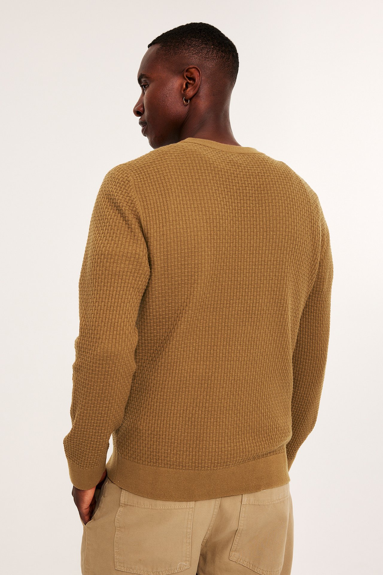Ryggbilde av en mann i brun strukturstrikket bomullsgenser med beige bukser.