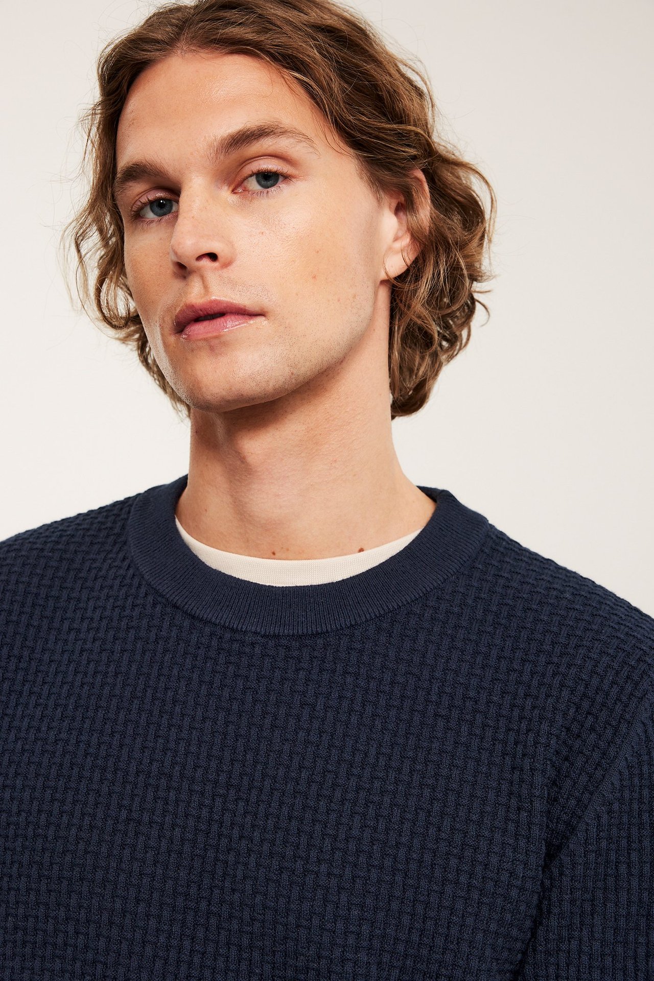 Nærbilde forfra av en mann i mørk blå strukturstrikket bomullsgenser over en lys t-skjorte.