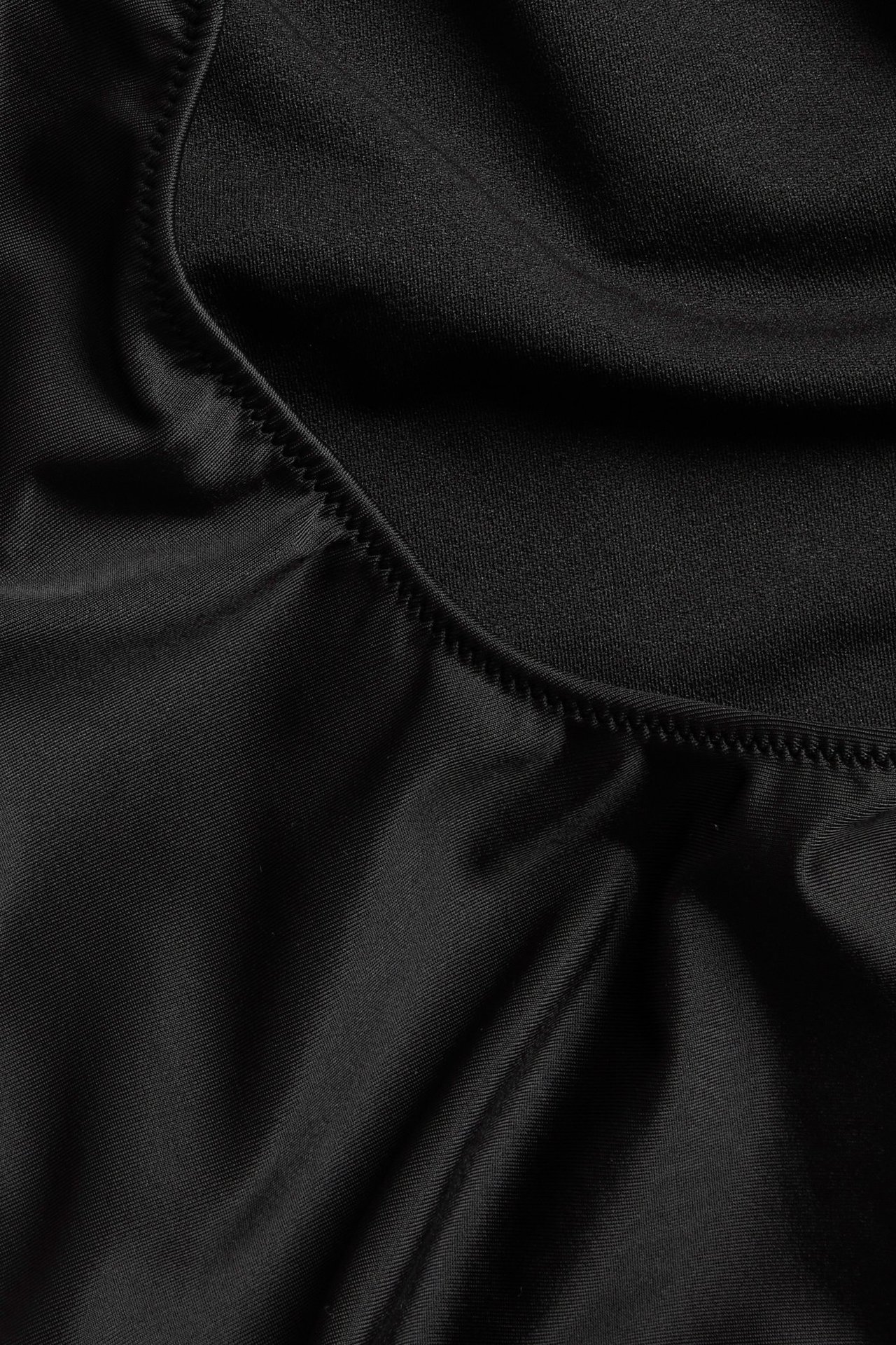 Lähikuva mustasta uimapuvun kankaasta, jossa näkyy siksak-tikkaus kaarevaa saumaa pitkin.
