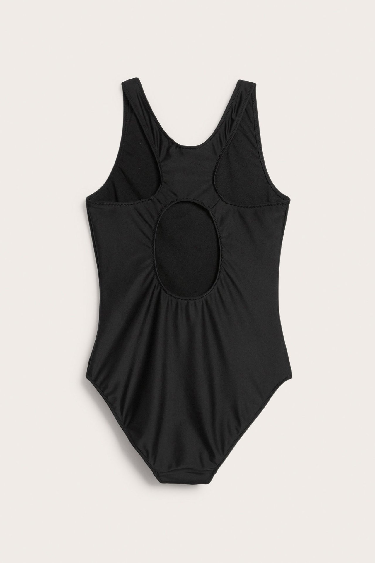 Selkäkuva yksivärisestä mustasta uimapuvusta leveämmillä olkaimilla ja pyöreällä leikkauksella takana.