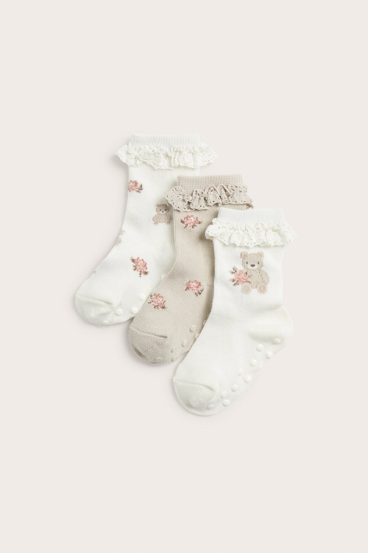 Tre par babysokker: offwhite og beige med bjørne-, rosemotiv, blondekanter og antiskli-såler.