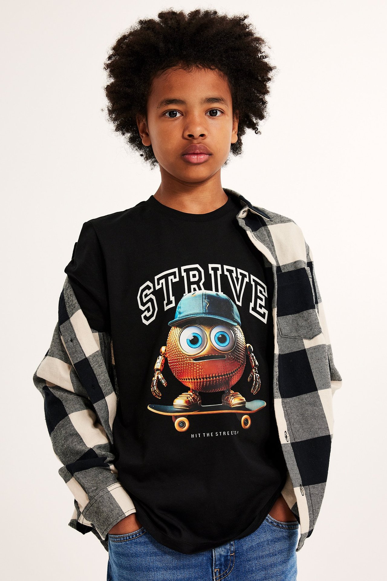 Widok z przodu dziecka w czarnym T-shircie z nadrukiem, koszuli w kratę i niebieskich dżinsach.