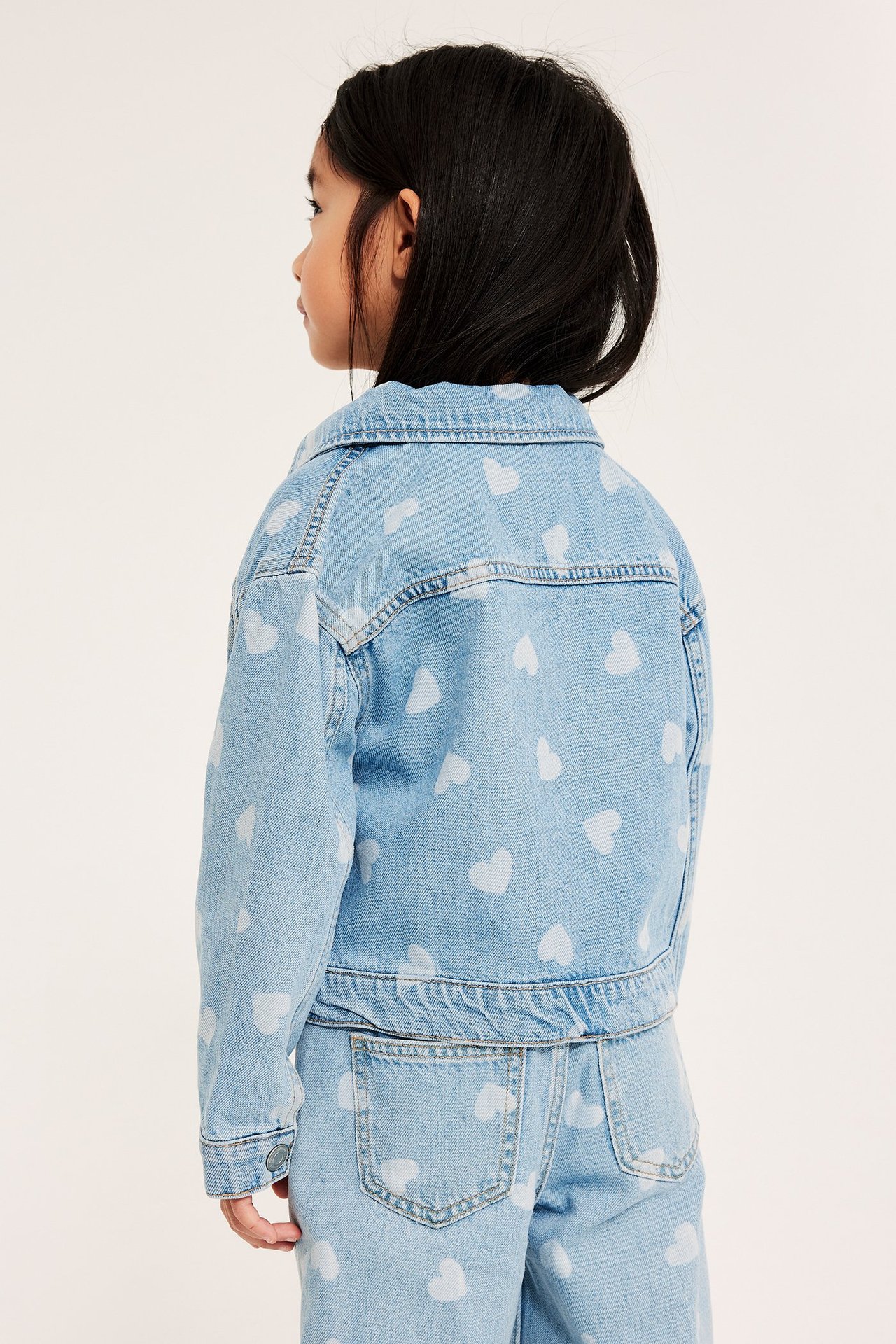 Sidevisning av et barn i en lyseblå dongerijakke med hvite hjertemønster og matchende jeans.