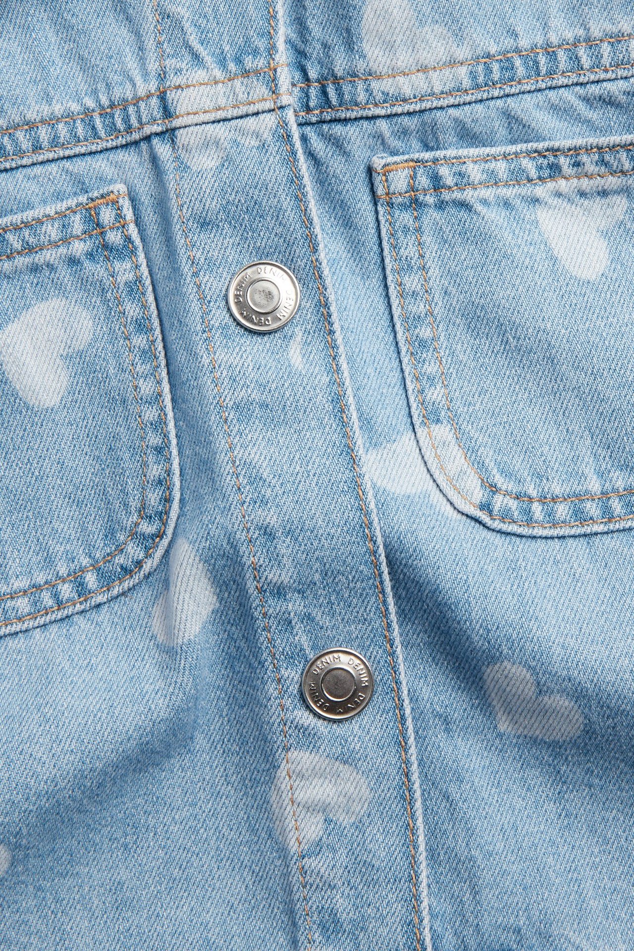 Lähikuva edestä: vaaleansininen lasten farkkutakki valkoisilla sydämillä, painonapeilla ja taskuilla.