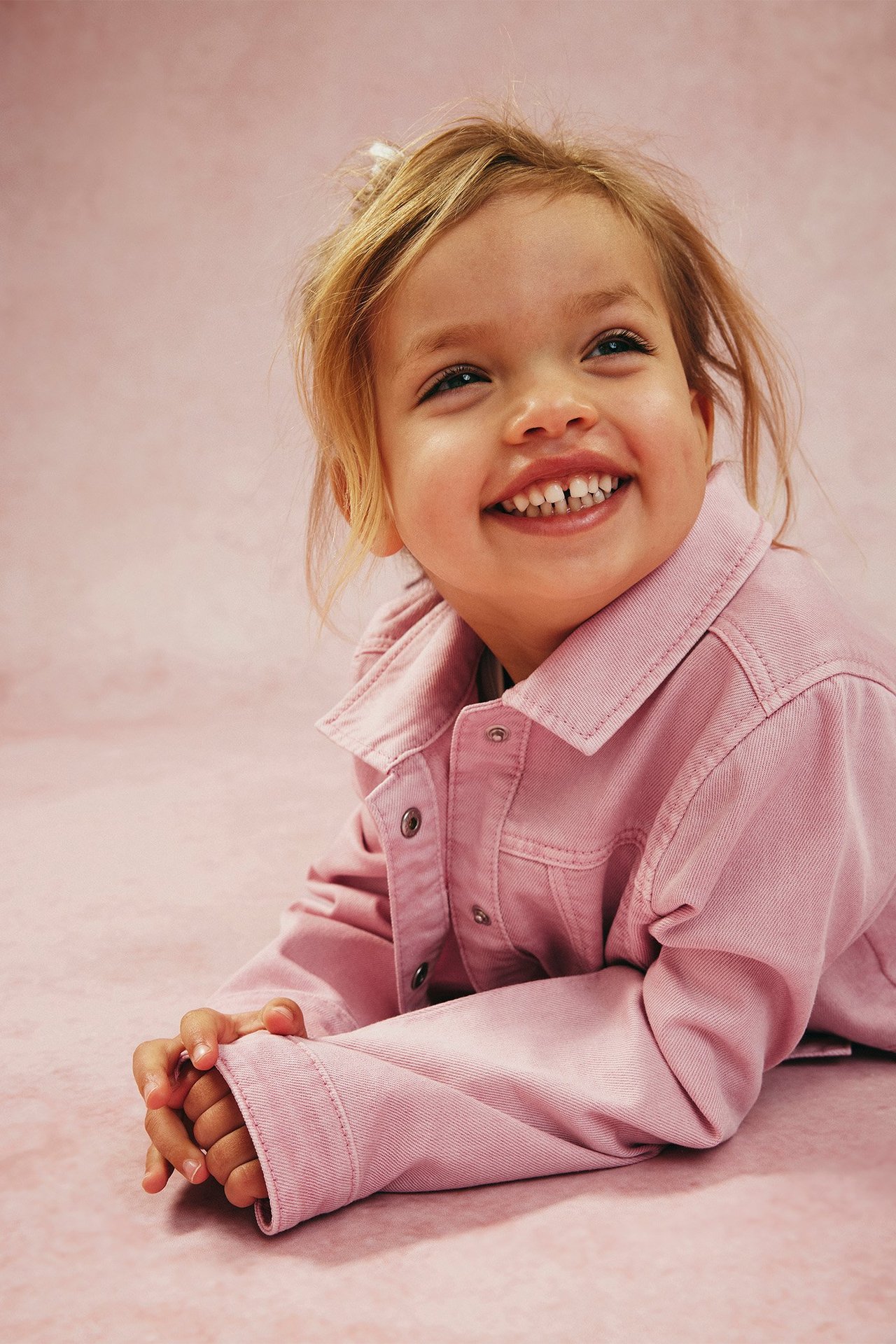 Närbild på ett leende barn i en ljusrosa jeansjacka med tryckknappar framtill.