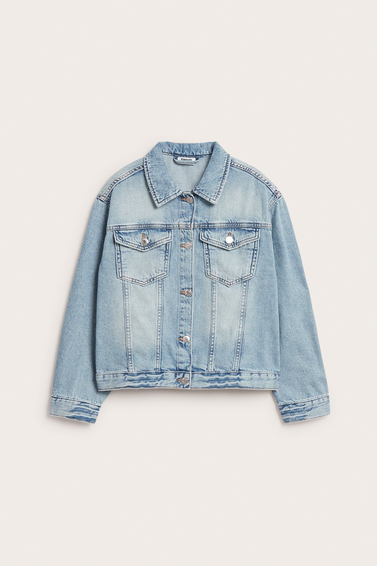 Framsida av en ljusblå oversized jeansjacka i bomull med silverknappar och bröstfickor.