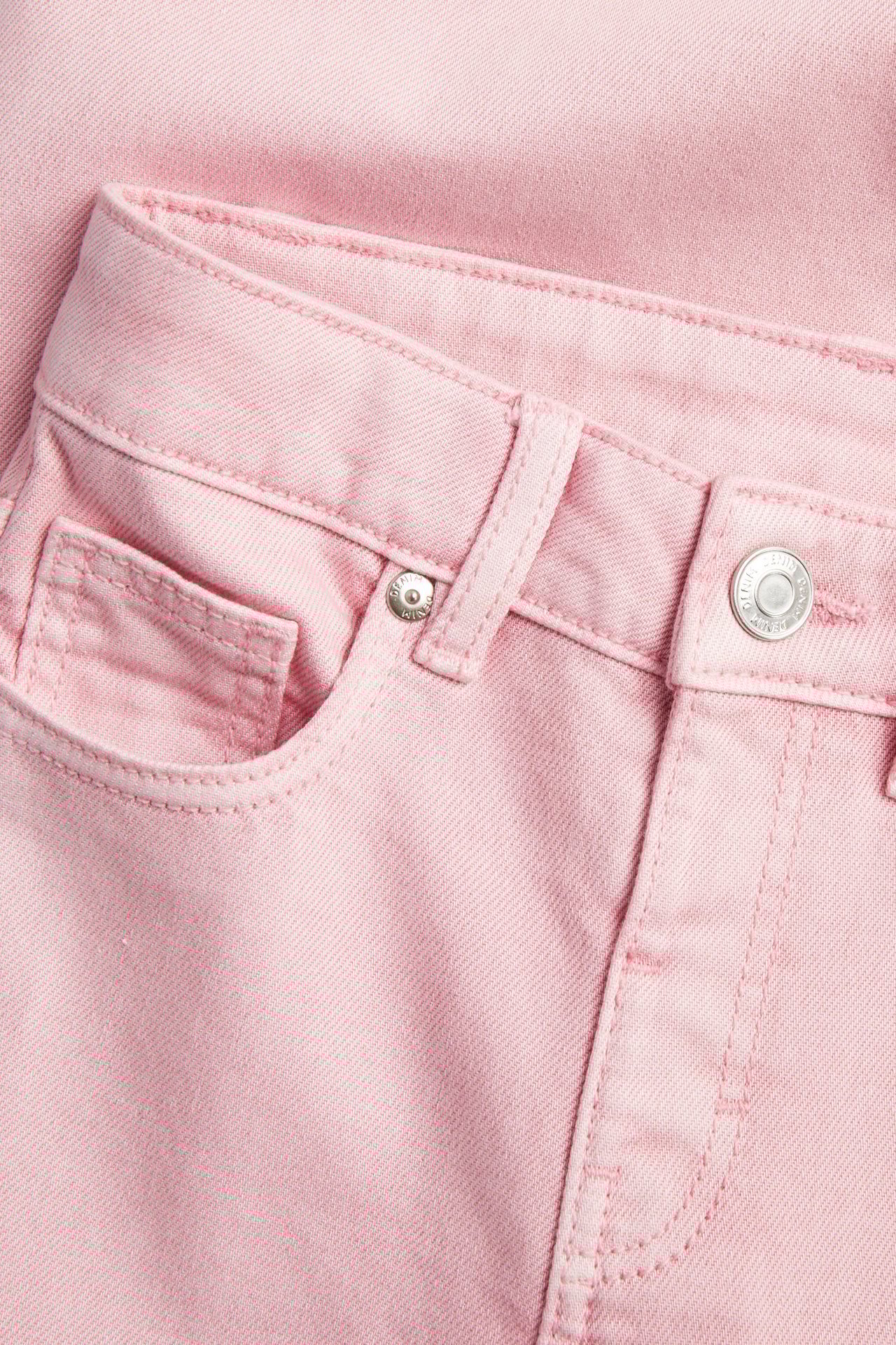 Nærbilde forfra av lysrosa bomullstwill-jeans med metalltrykknapp og frontlomme.