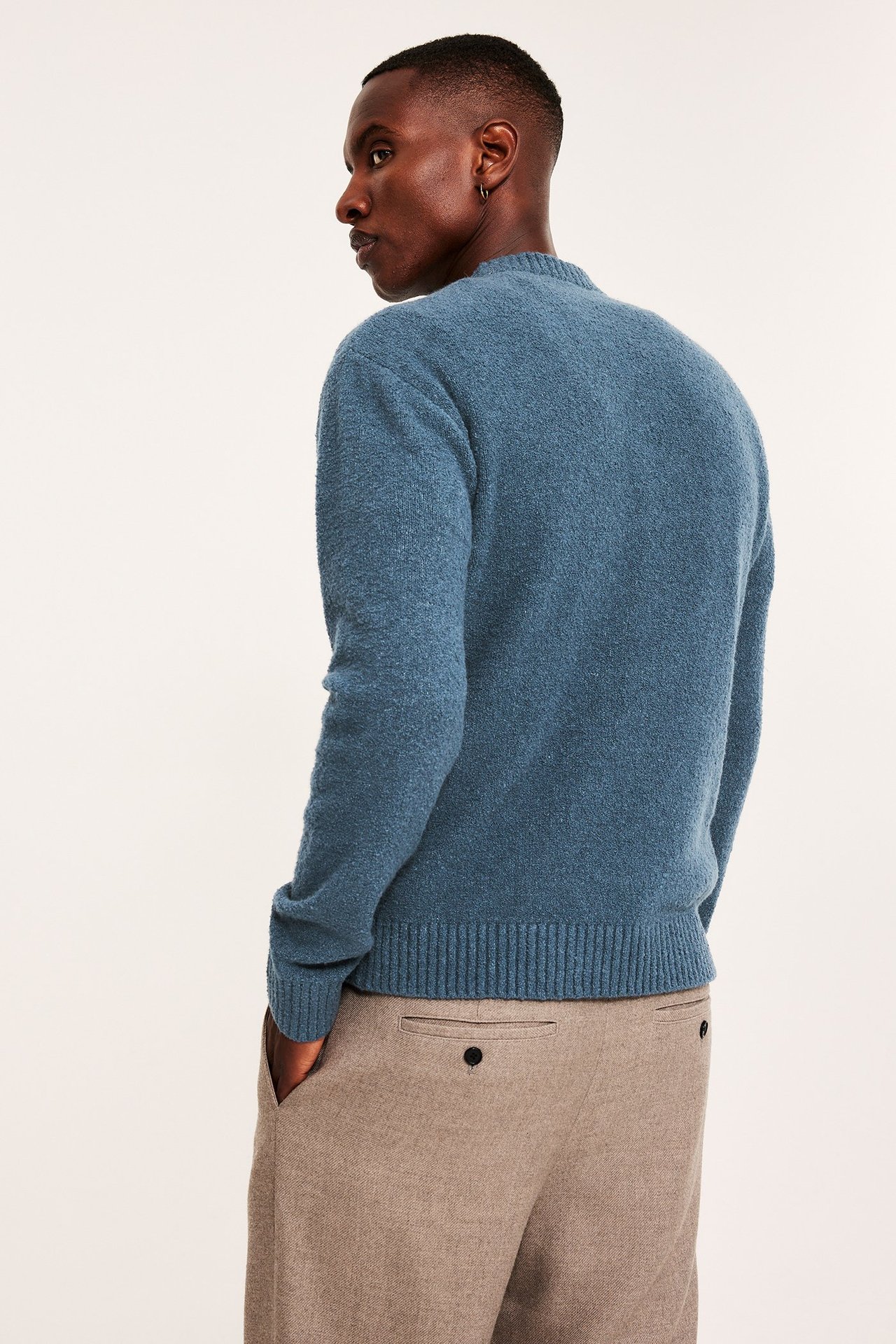 Widok z boku na mężczyznę w niebieskim teksturowanym swetrze i beżowych spodniach, z ręką w kieszeni.