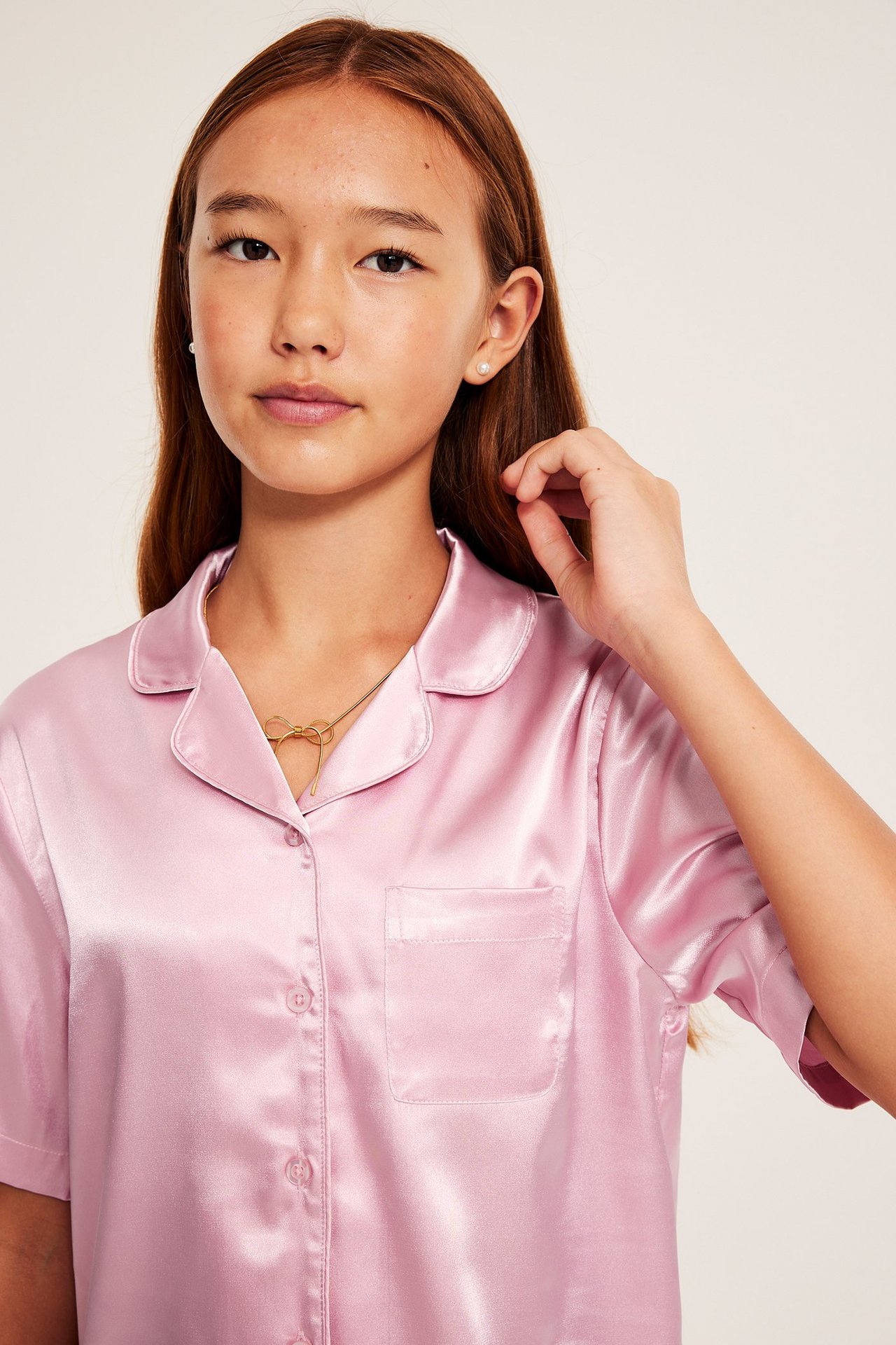 Lähikuva lapsesta vaaleanpunaisessa satiinisessa pyjamapaidassa, kultaisessa rusettikaulakorussa ja helmikorvakoruissa.